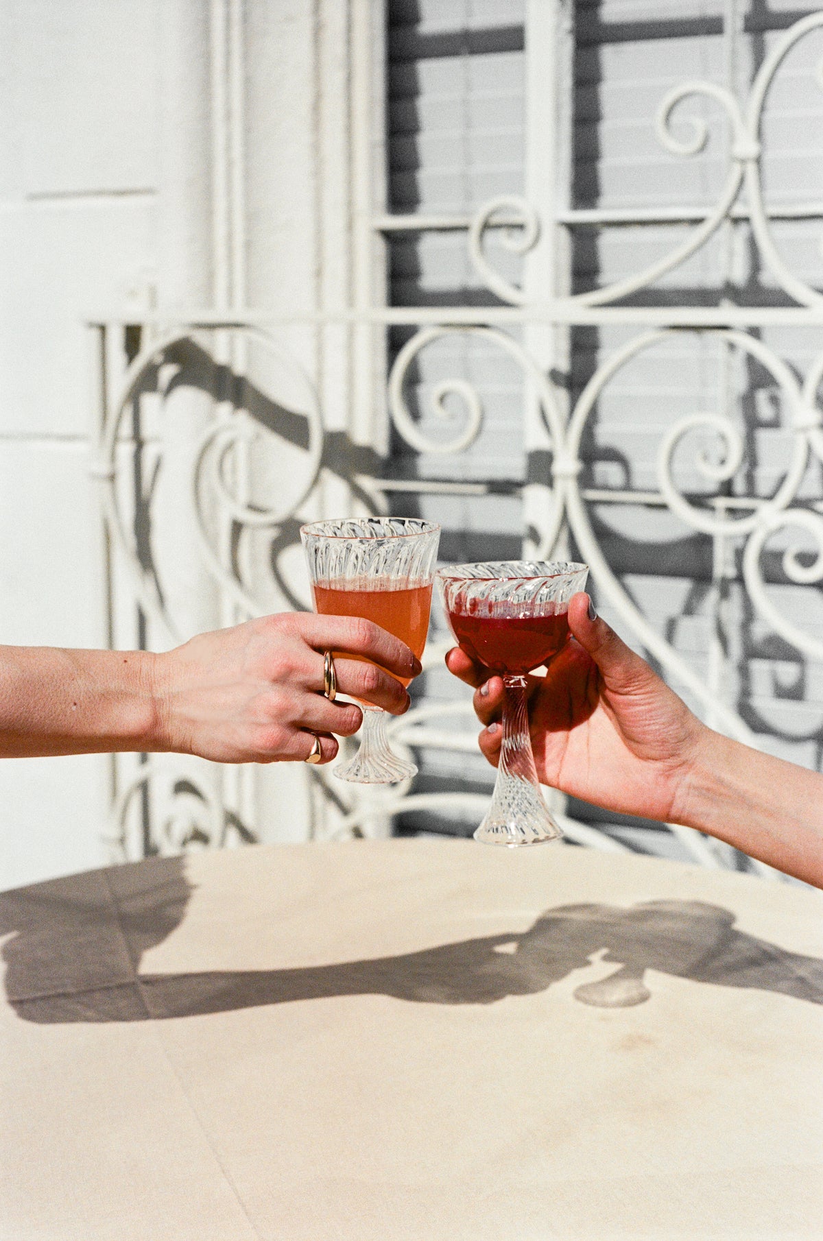 Models hold ribbed wine glass and champagne coupe filled with orange wine.