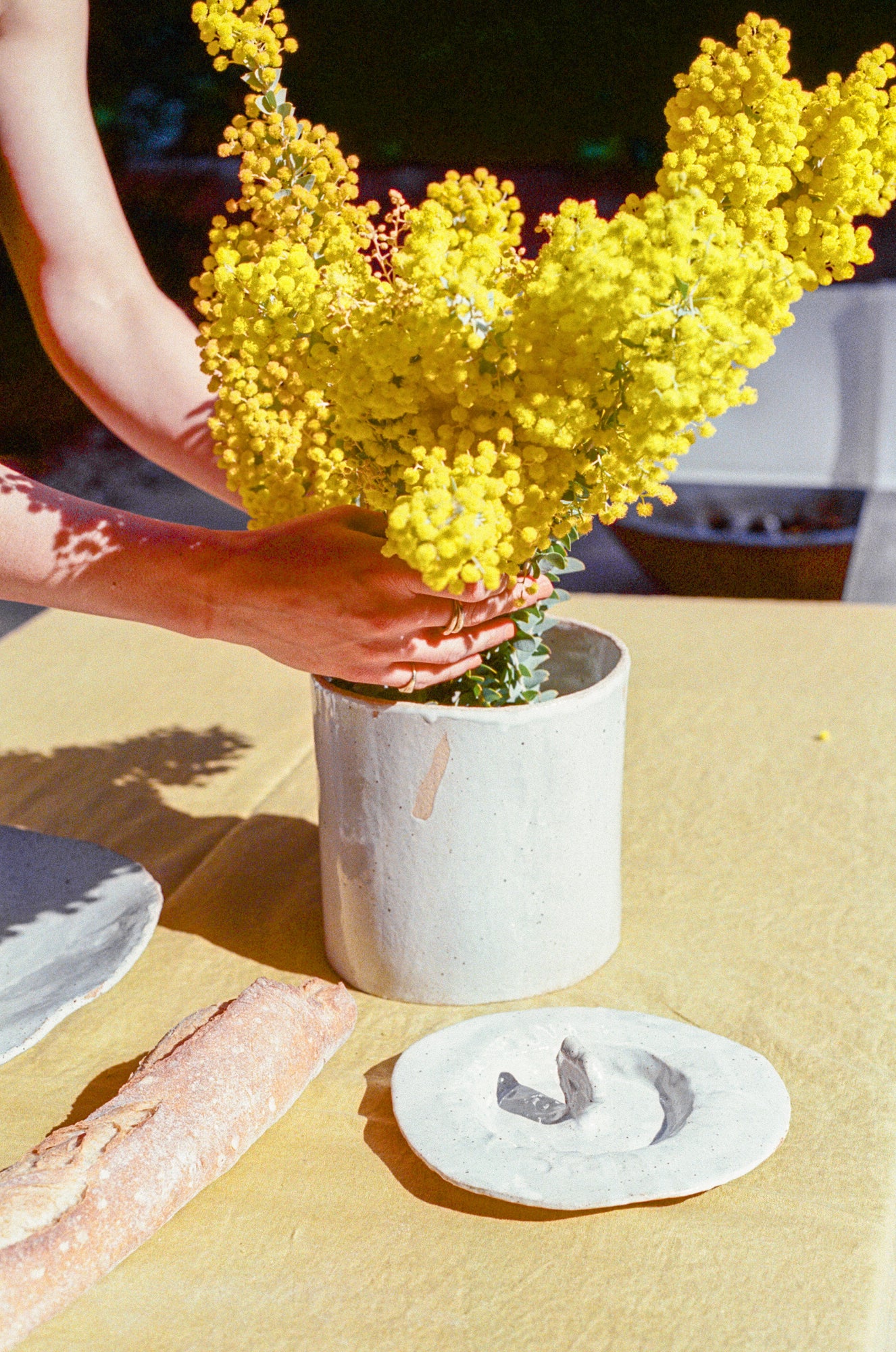 Model arranges flowers in large handbuilt ceramic jar with white glaze.