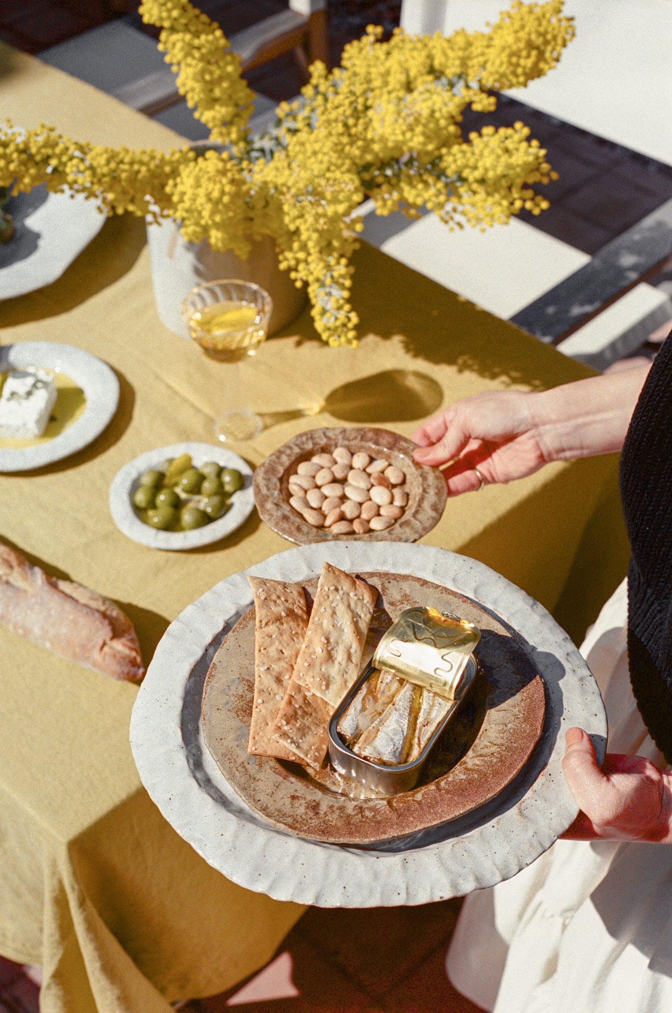 Model holds handmade ceramic plates in varying sizes and colors over tablescape with food.