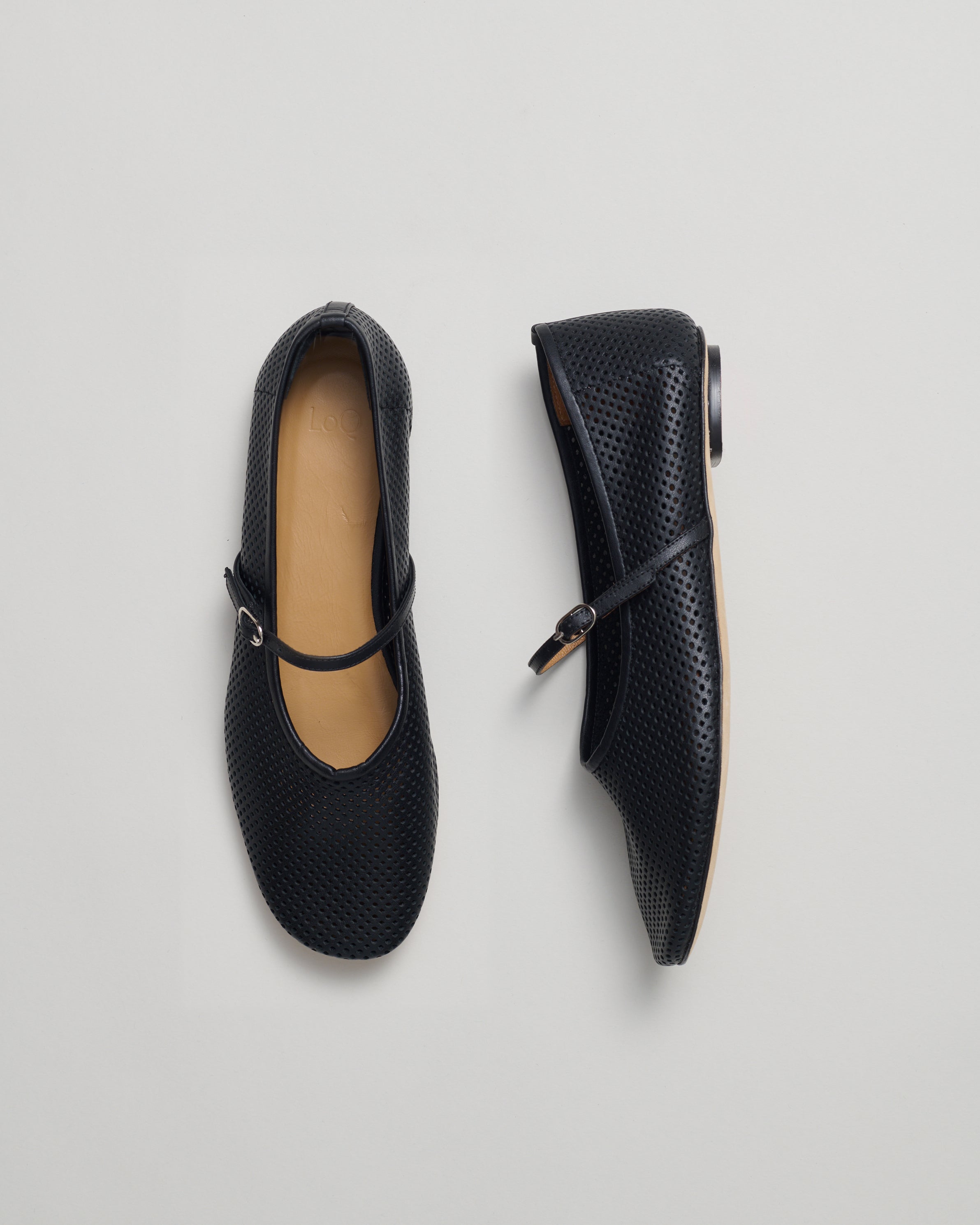 Pair of black ballet flats in perforated leather on a light gray background