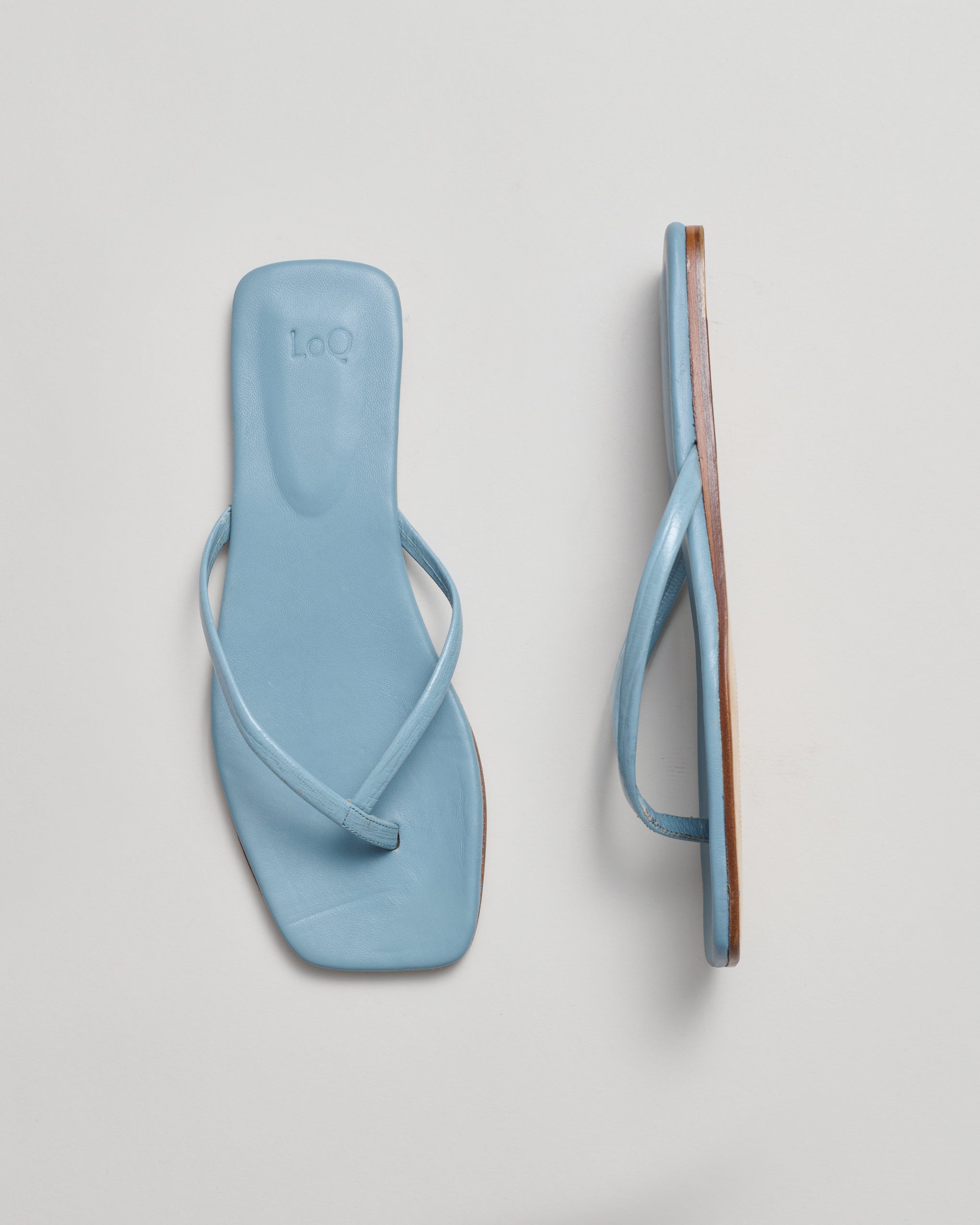 Pair of light blue minimalist sandals on a gray background
