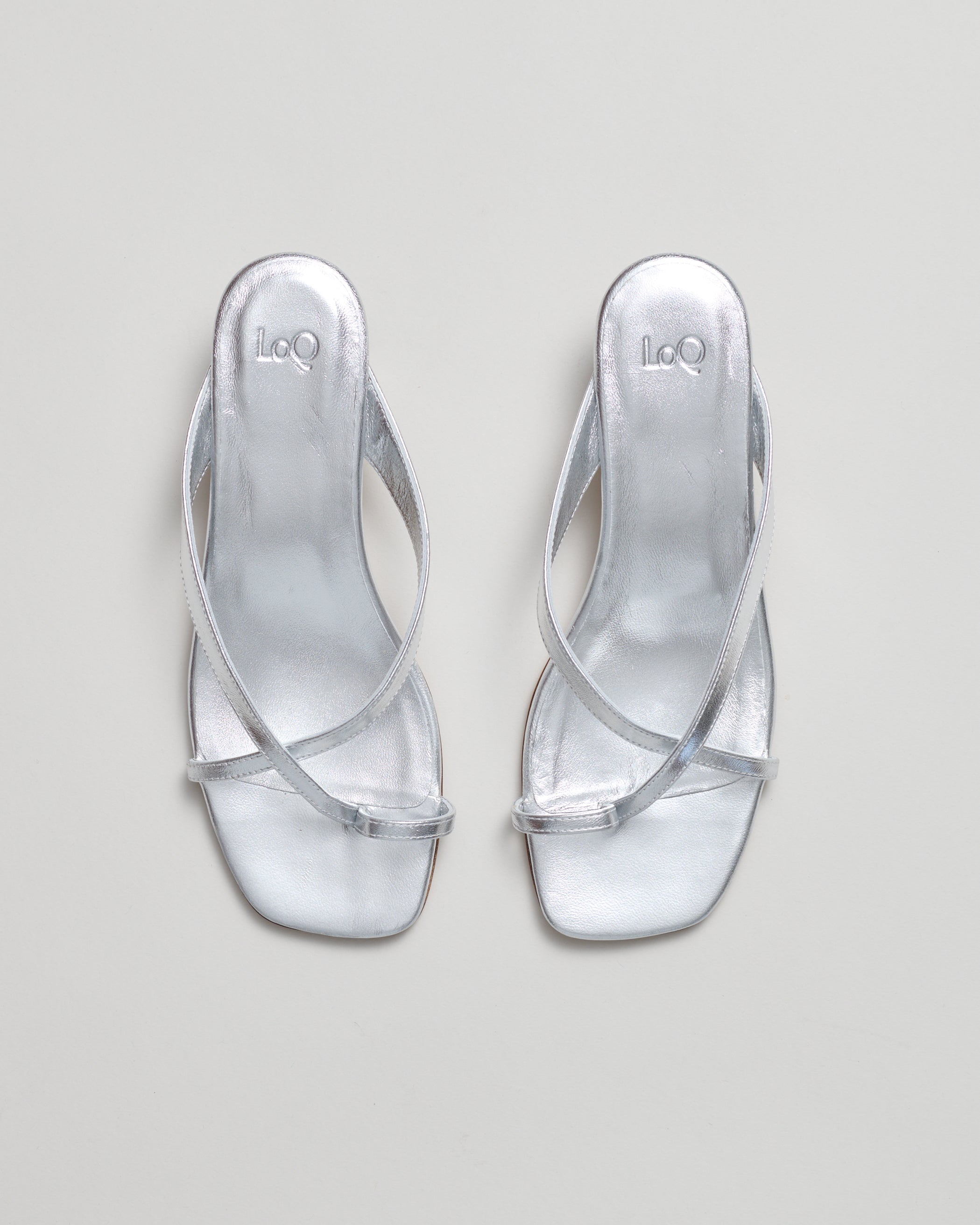 A pair of metallic silver strappy sandals with low block heels, shown from a top-down view on a light gray background.