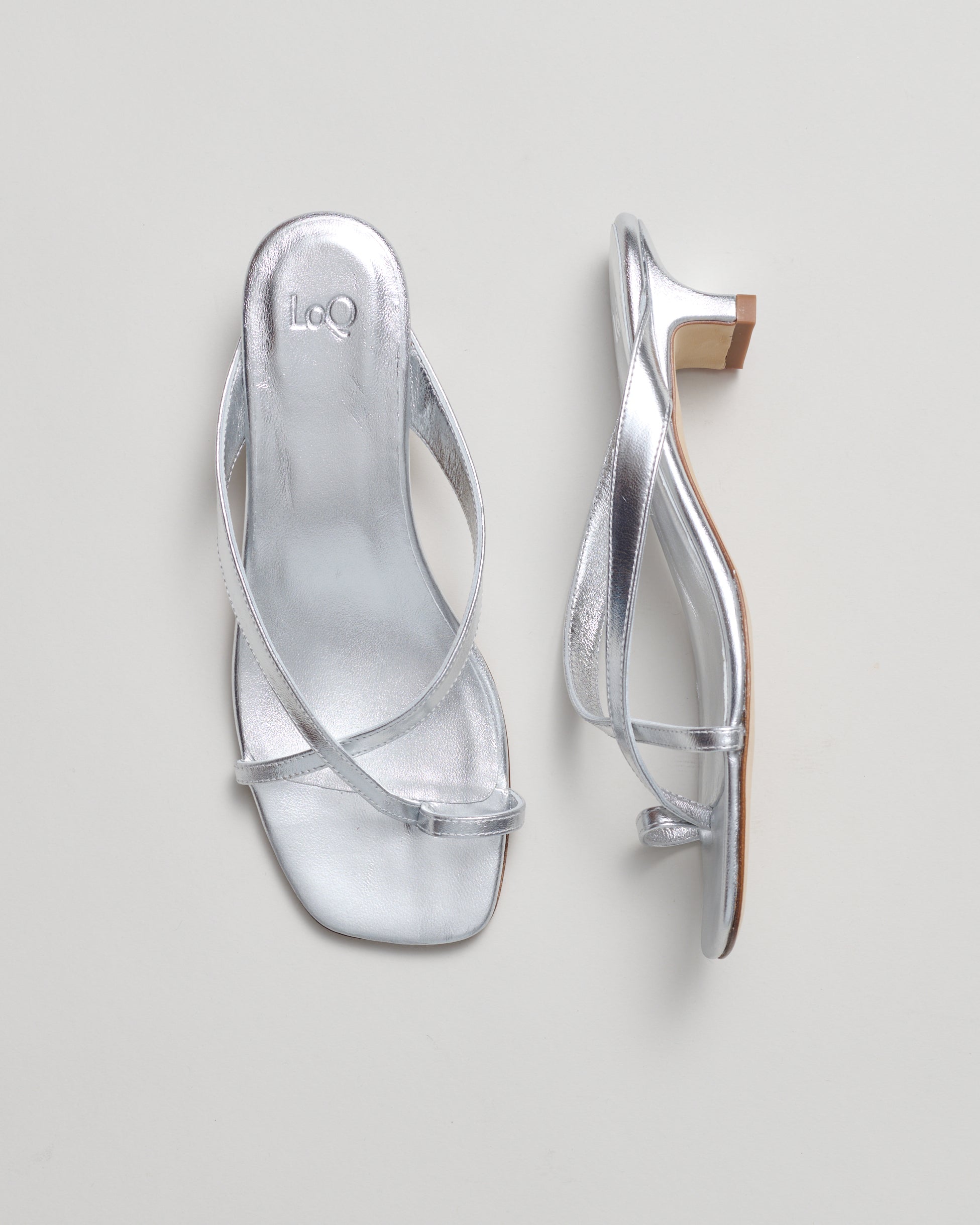 A pair of metallic silver strappy mule sandals shown from top and side views on a light gray background.