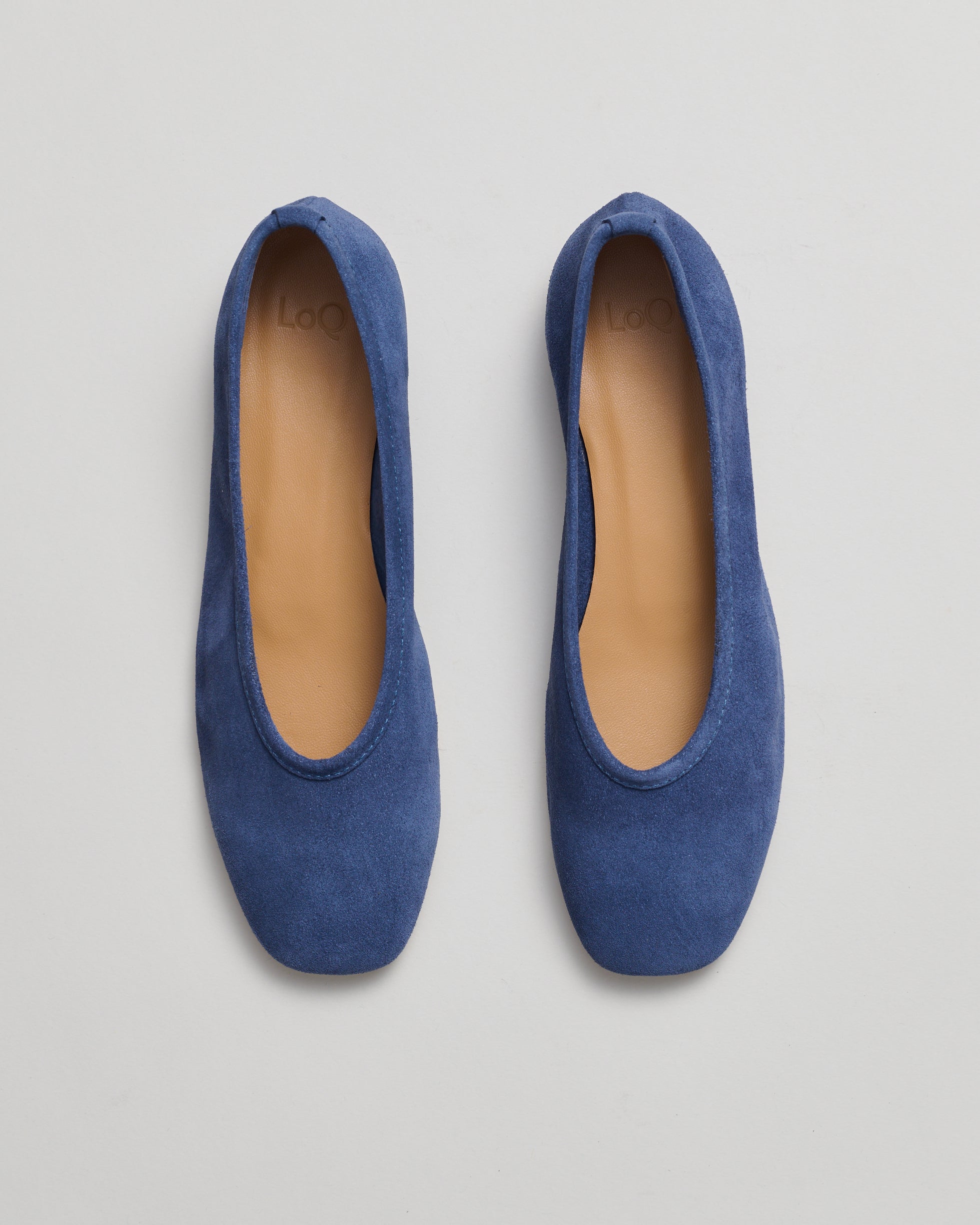 A pair of blue suede ballet flats with tan interiors, shown from a top-down view on a light gray background.