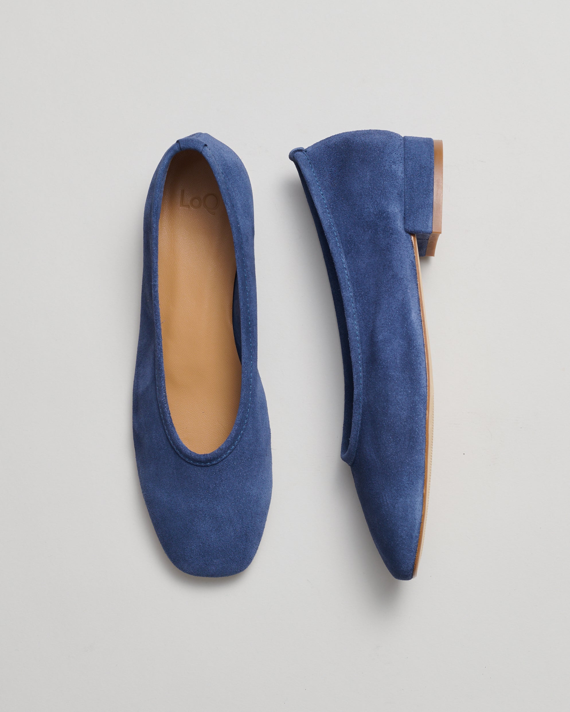 A pair of blue suede ballet flats shown from top and side views on a light gray background.