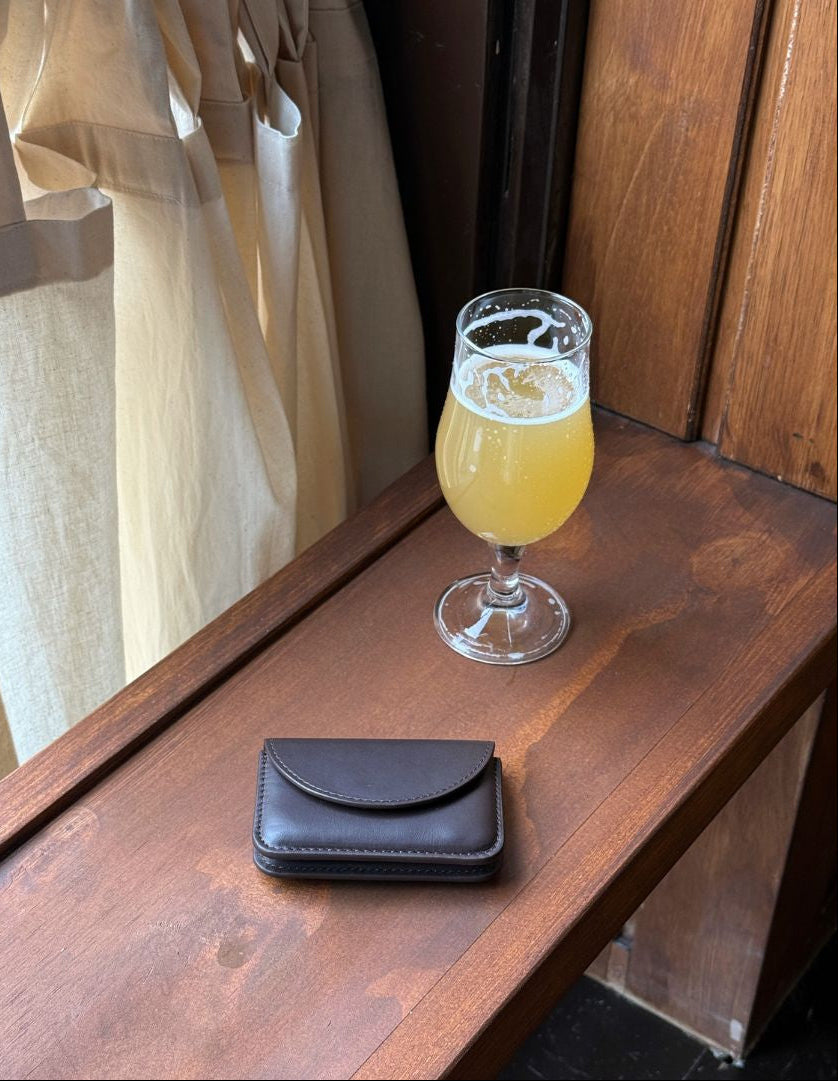 Glass of beer and brown wallet on a wooden surface with a window in the background