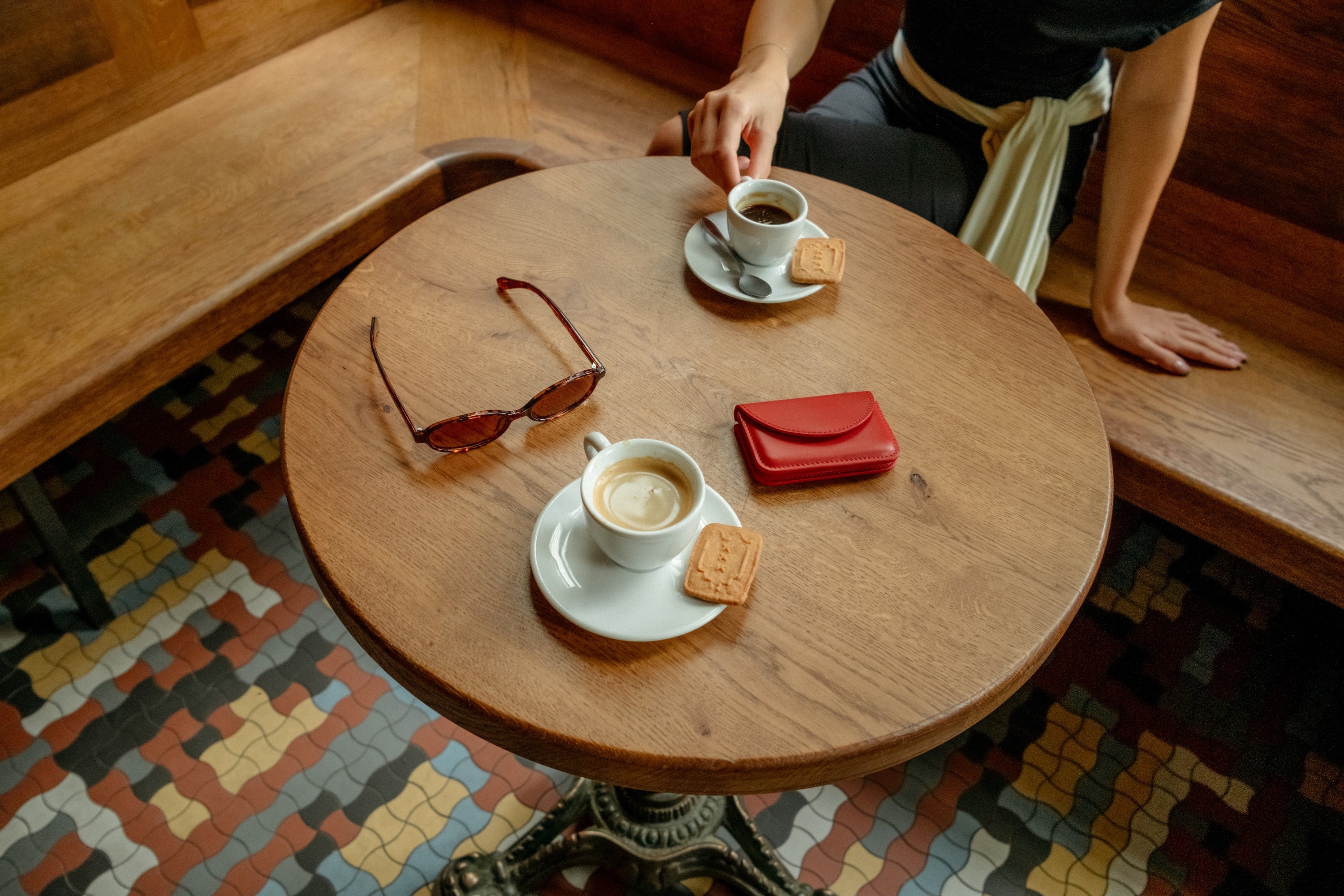 Person sitting at a wooden table with coffee, cookies, sunglasses, and a red wallet.