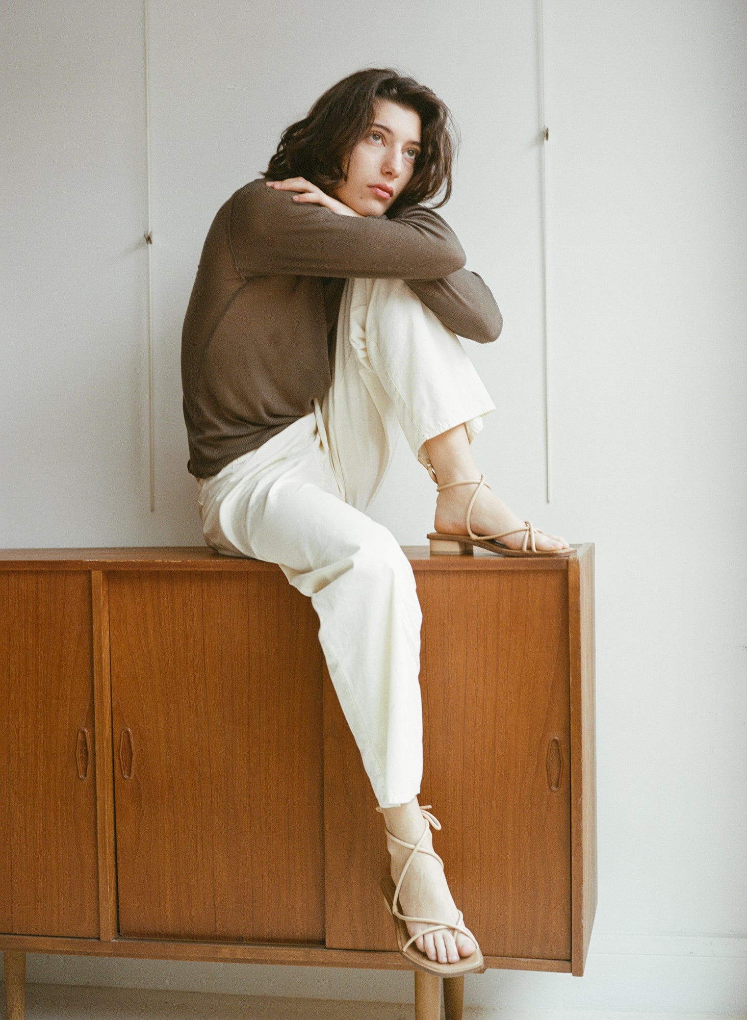 Model wears light beige sandals with tubular straps that cross the top of the feet and wrap around the ankles to tie.