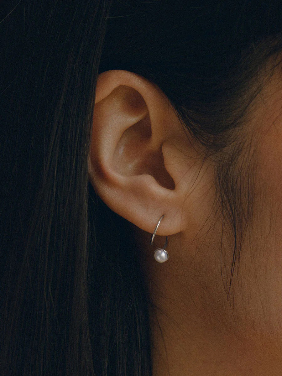 Model wears sterling silver earring that wraps through piercing around lobe with a small pearl adornment.