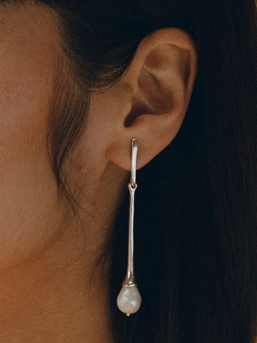 Model wears long sterling silver drop earring with large pearl at the bottom.