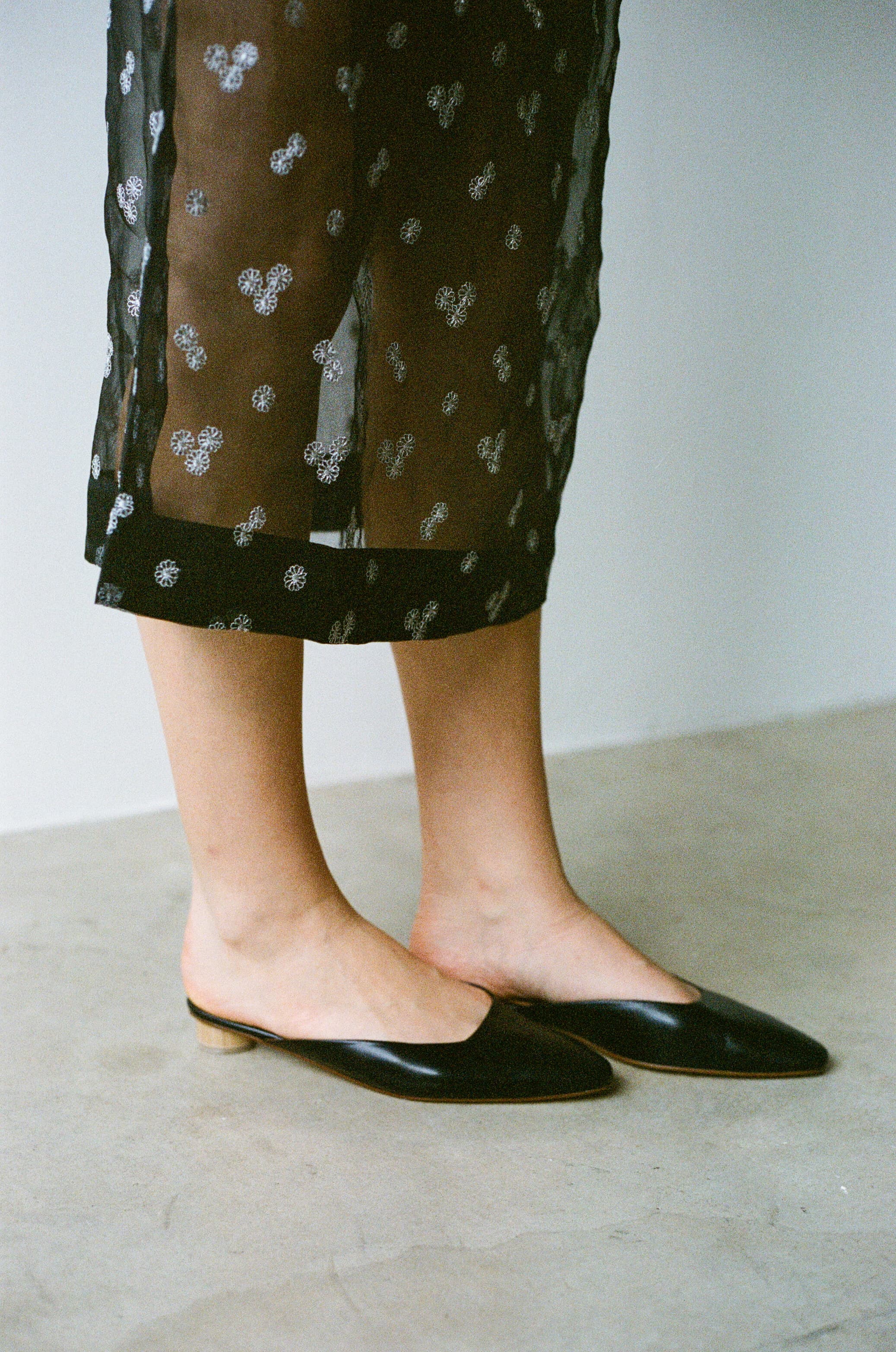 Person wearing black flat shoes and a patterned skirt on a neutral background