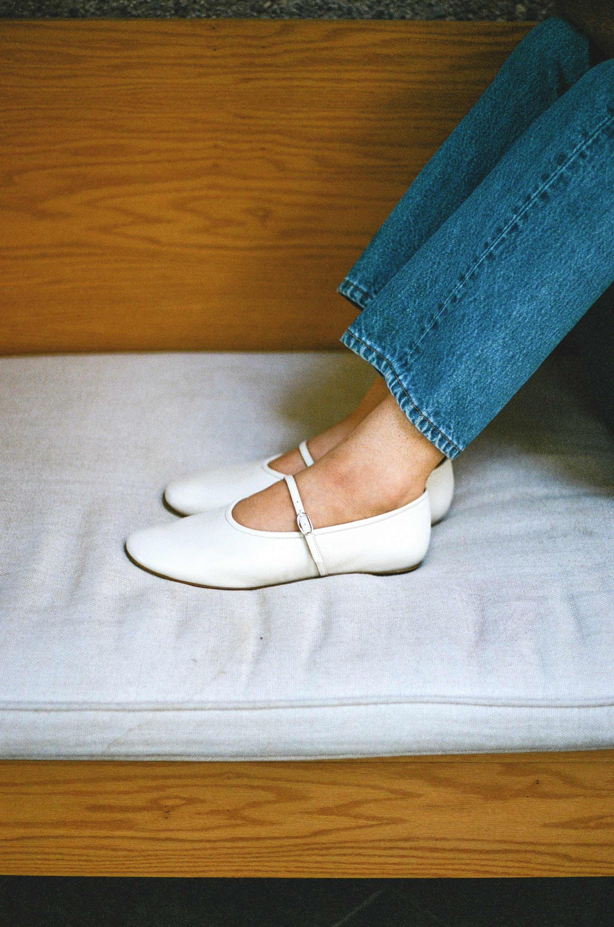 Model wears off white colored leather mary jane style flat shoe with strap and buckle closure.