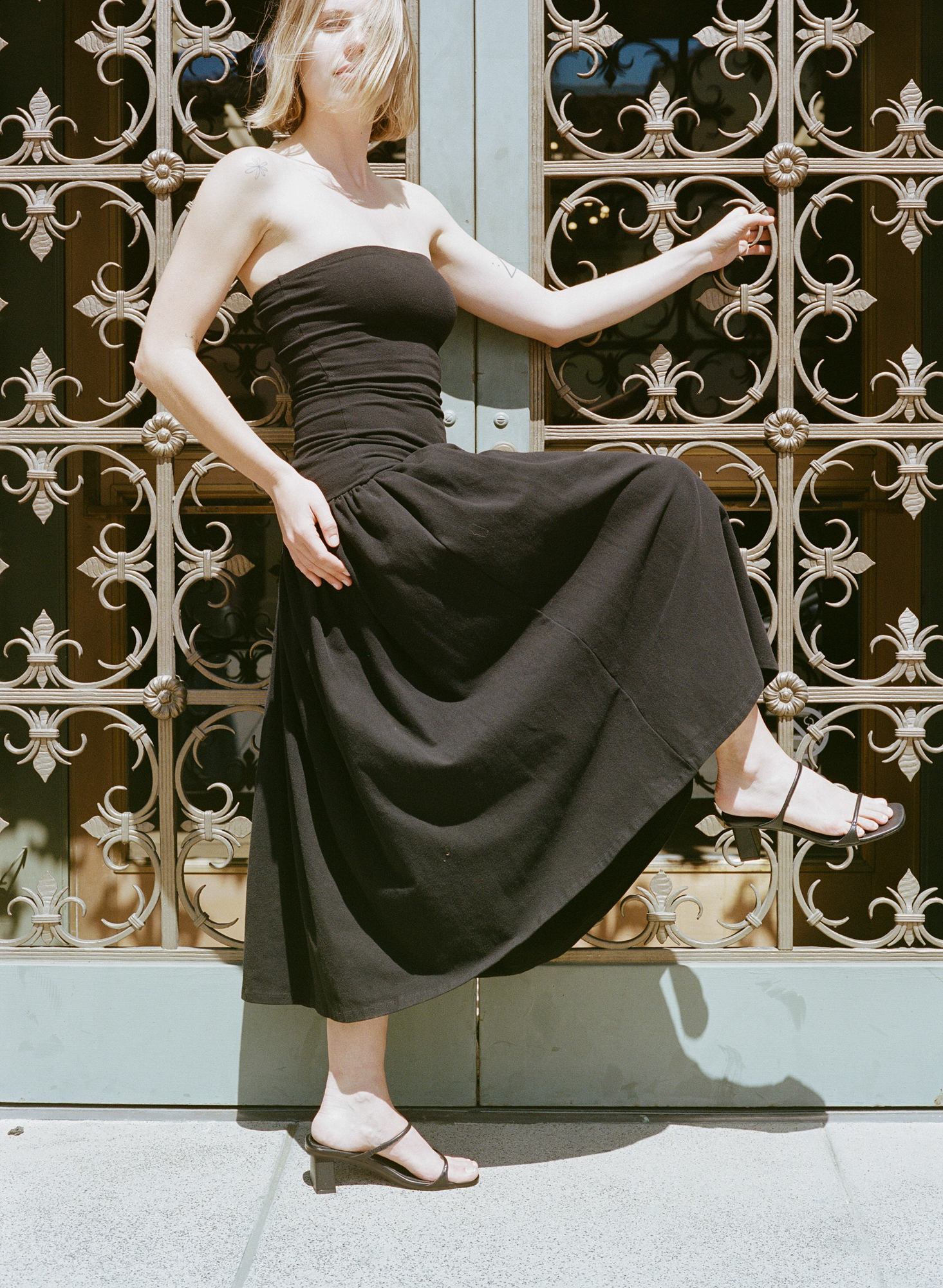 Model wears black heeled leather sandal featuring two thin straps and square block heel.