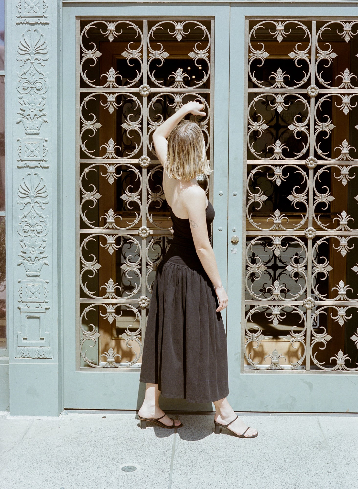 Model wears black heeled leather sandal featuring two thin straps and square block heel.