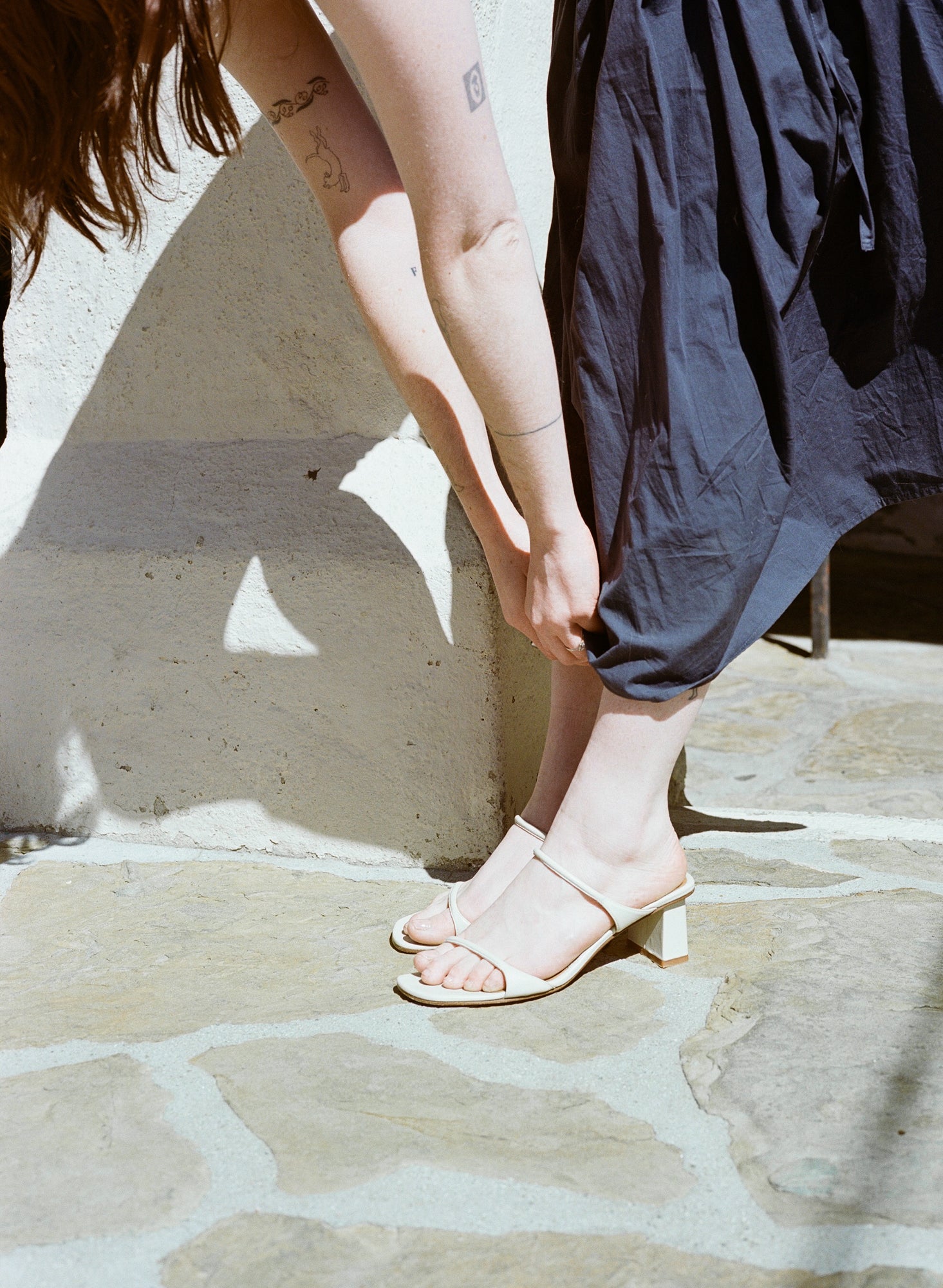 Model wears off white heeled leather sandal featuring two thin straps and square block heel.