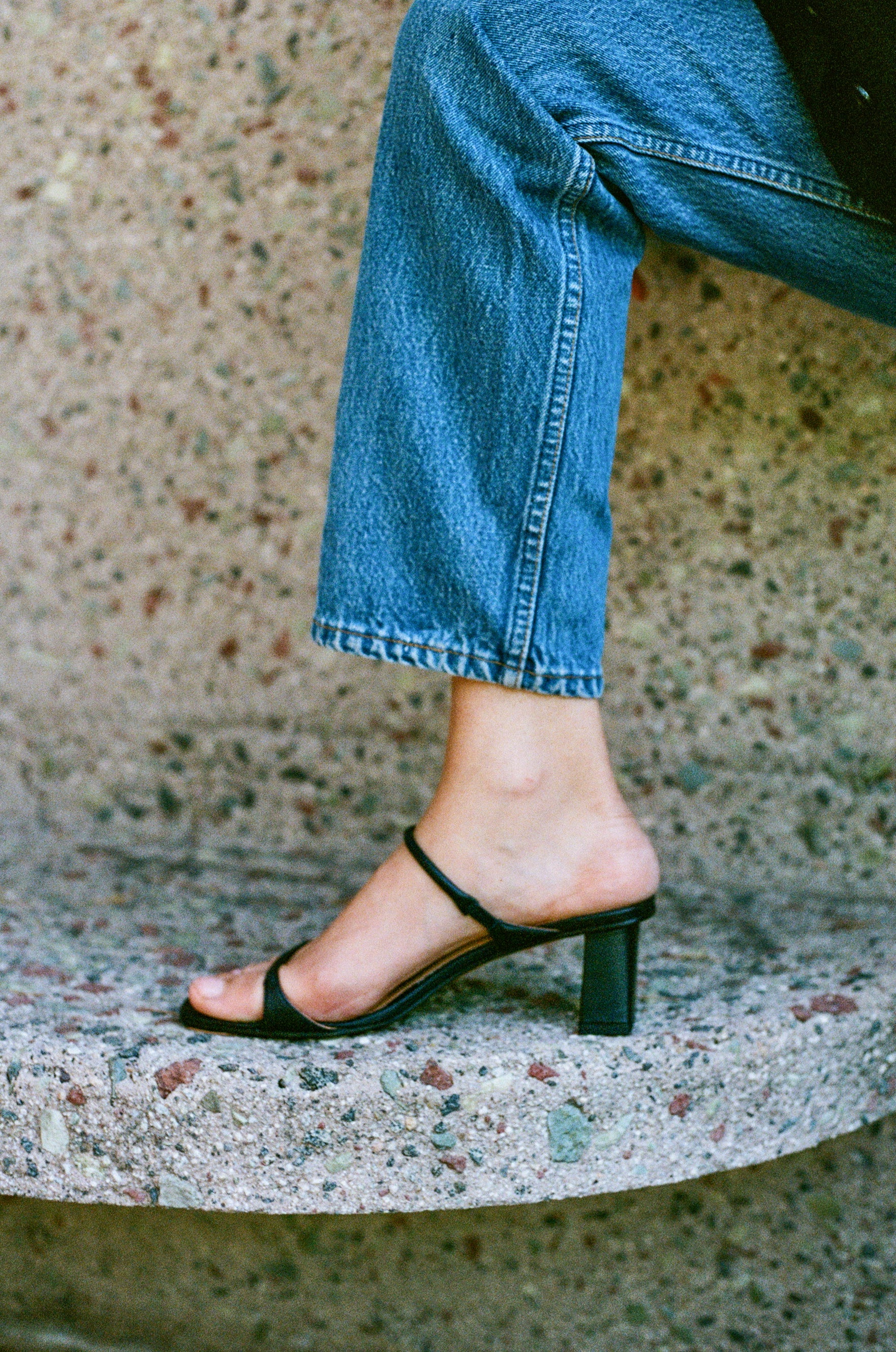 Model wears black leather sandal featuring two thin straps and square block heel.