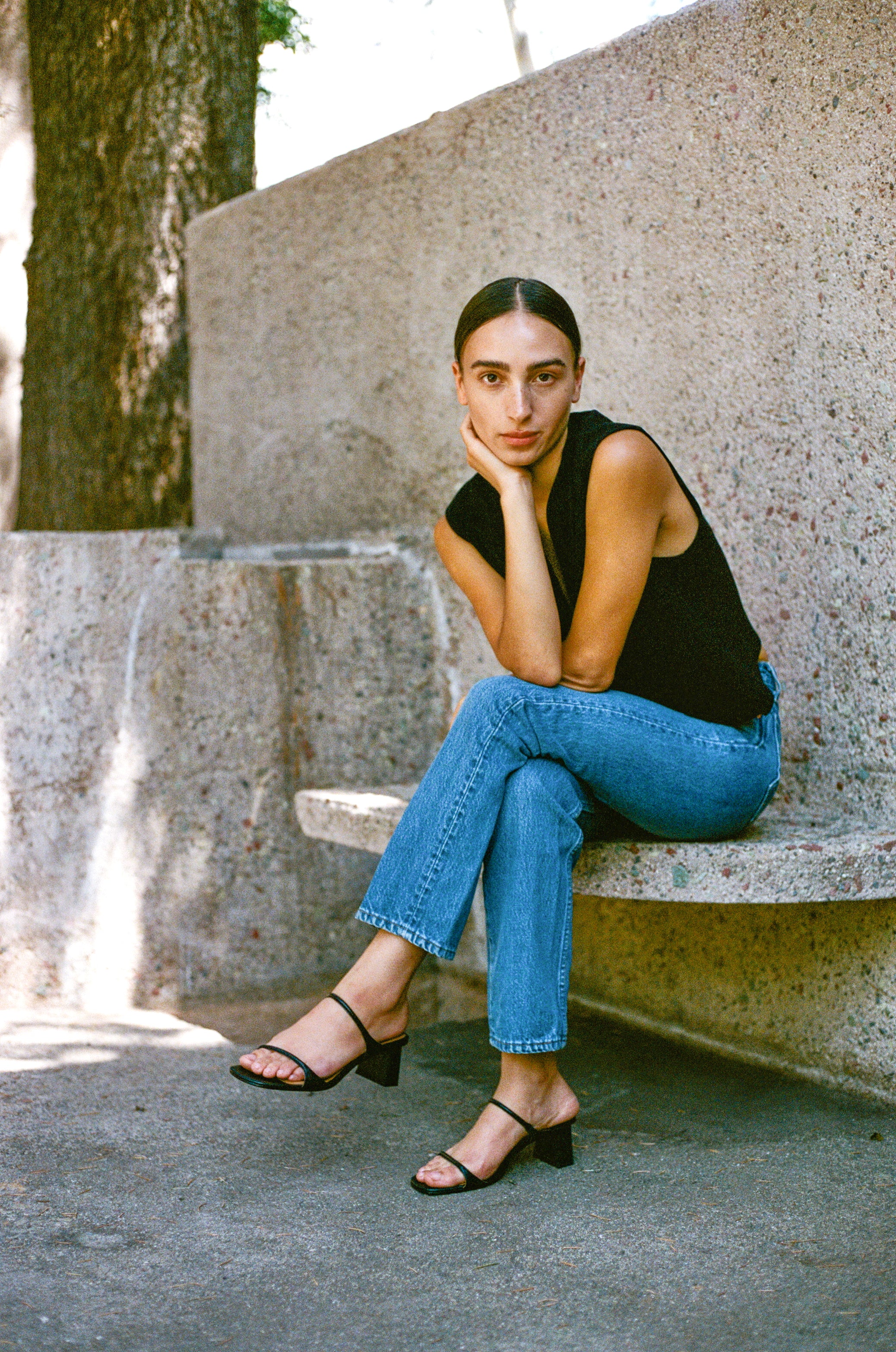 Model wears black leather sandal featuring two thin straps and square block heel.