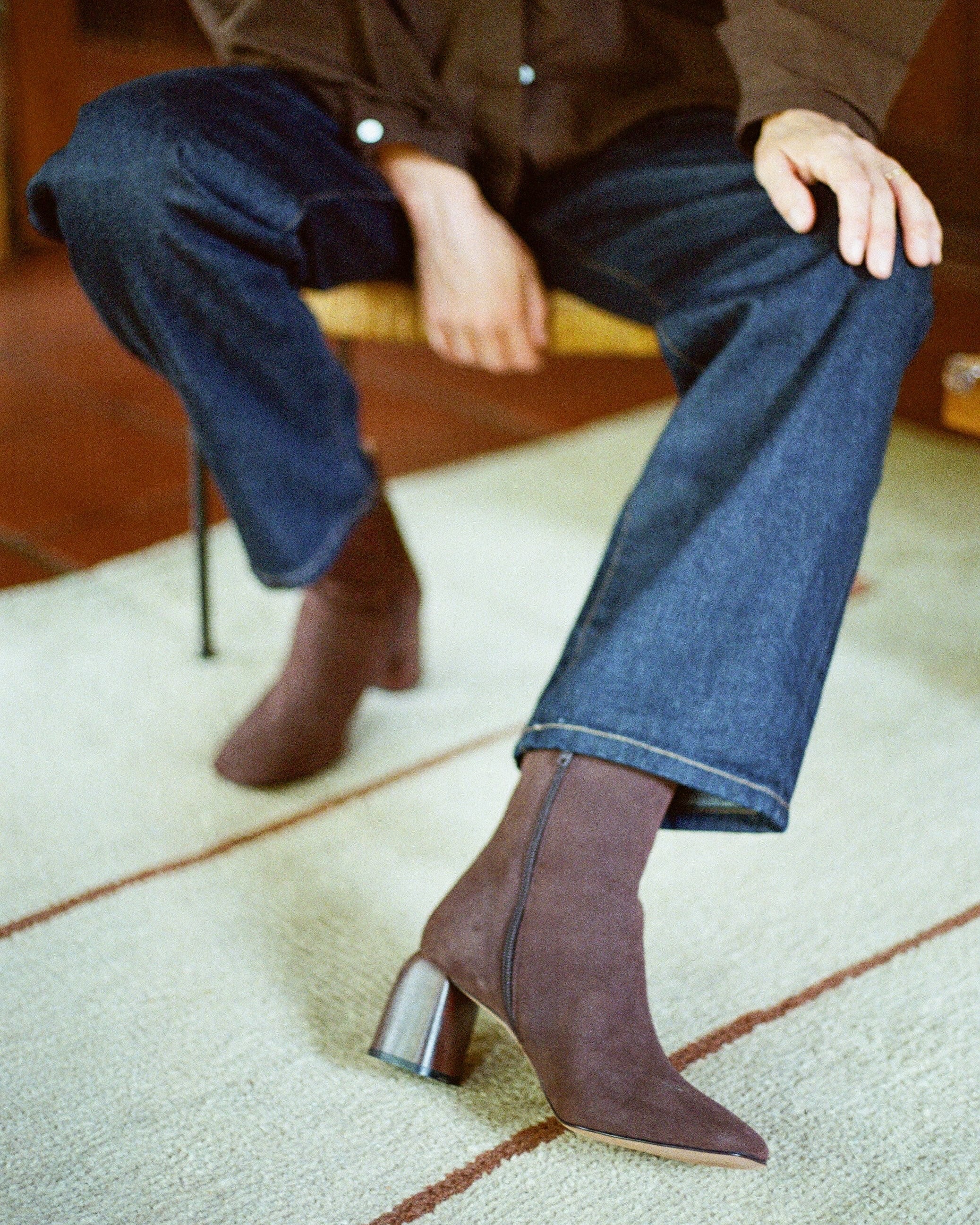 Person wearing brown suede ankle boots and blue jeans sitting on a chair.