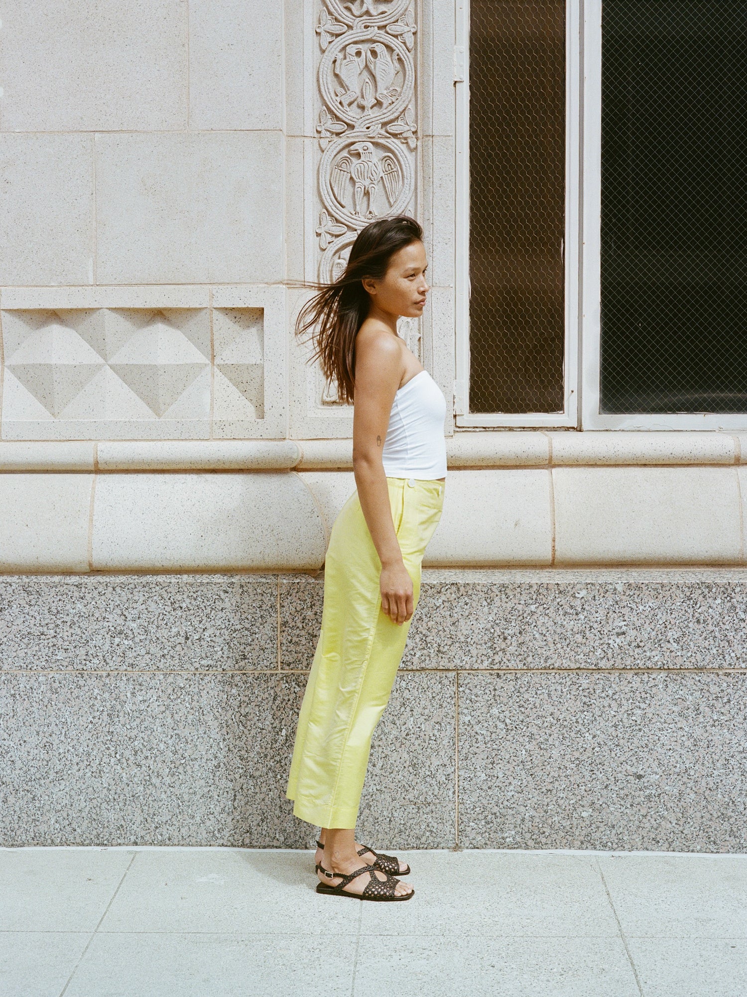 Model wears flat black leather sandals with lattice woven upper and slingback buckle.