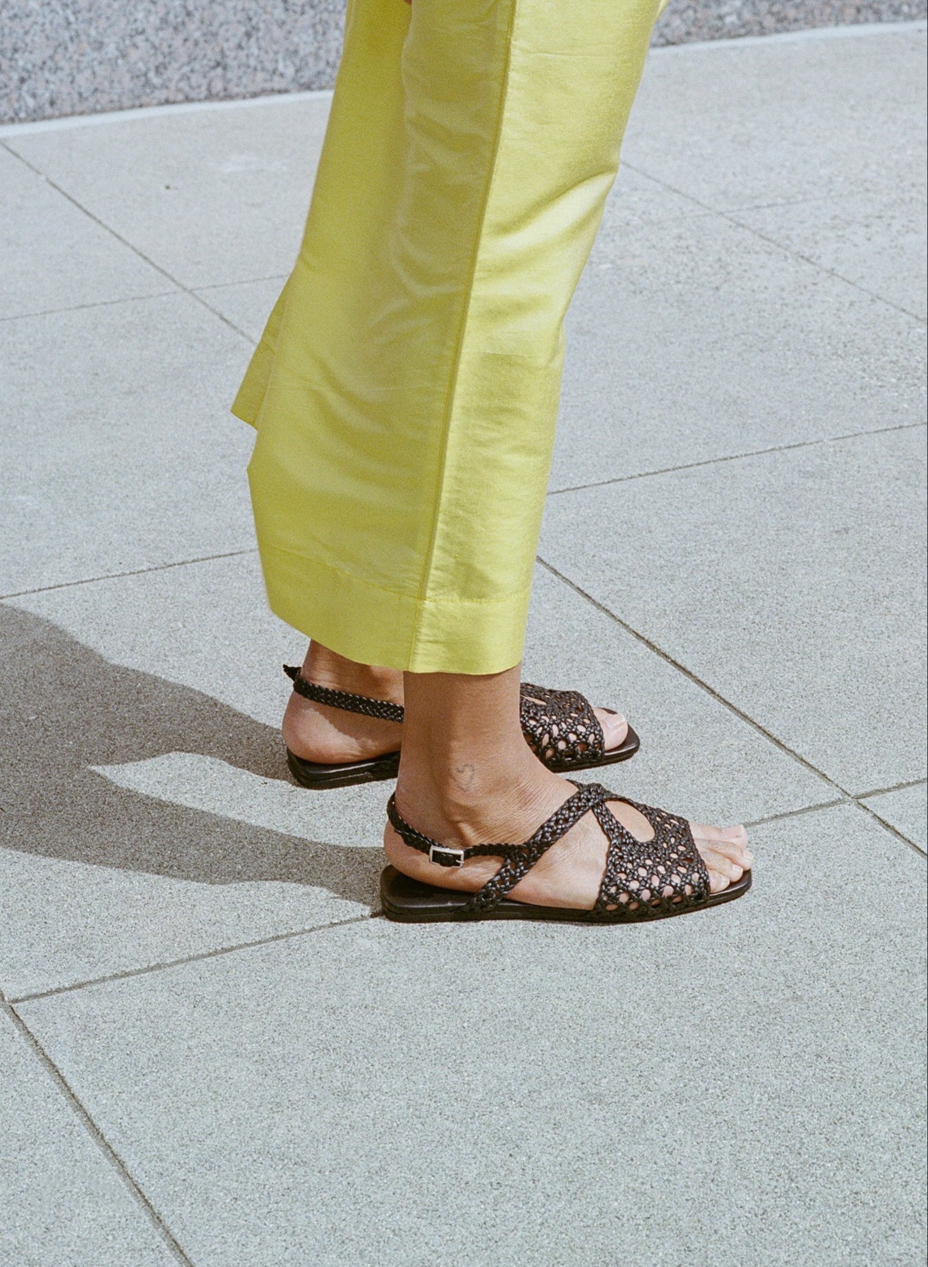 Model wears flat black leather sandals with lattice woven upper and slingback buckle.