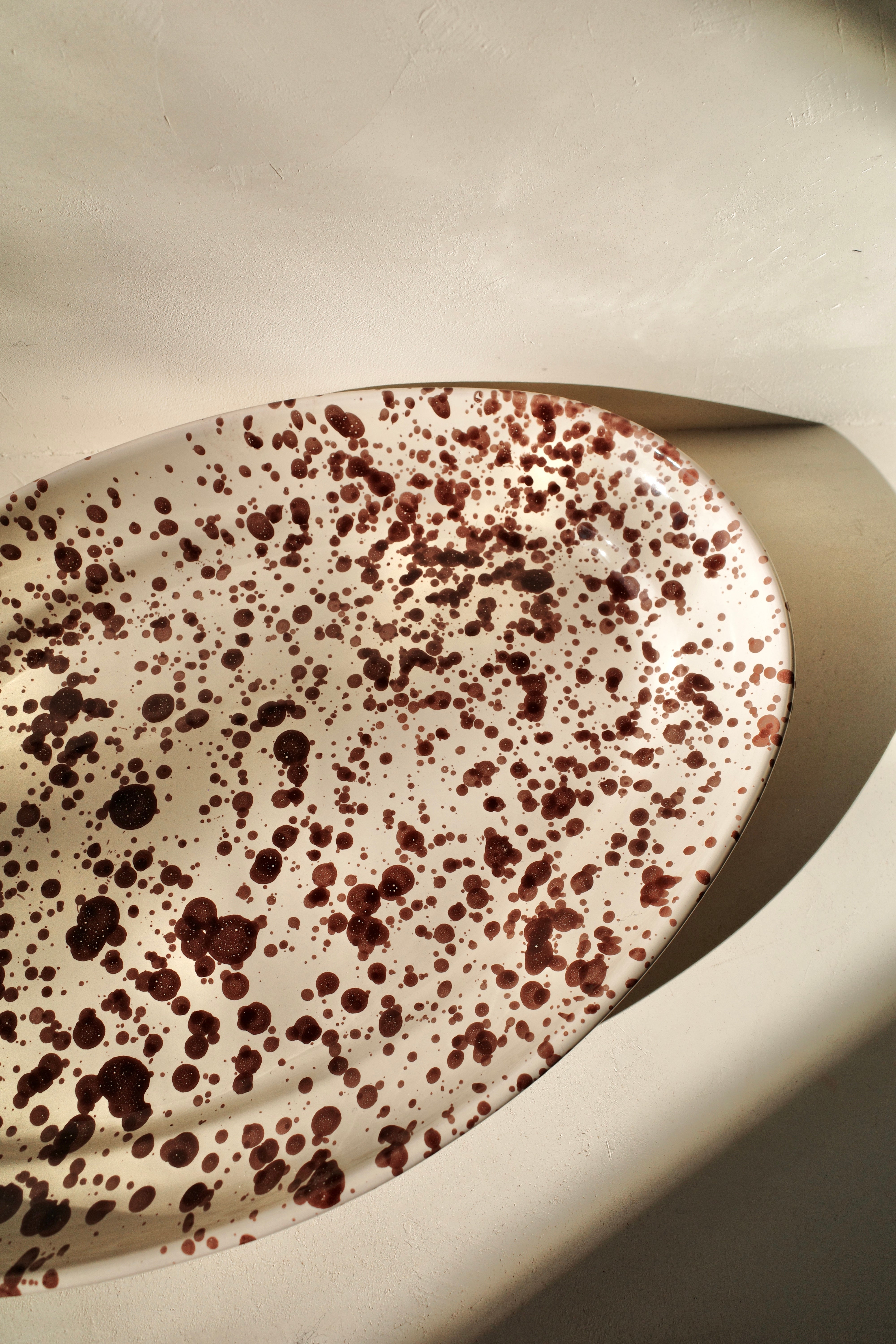 Ceramic platter with white glaze and dark brown paint splatter pattern.