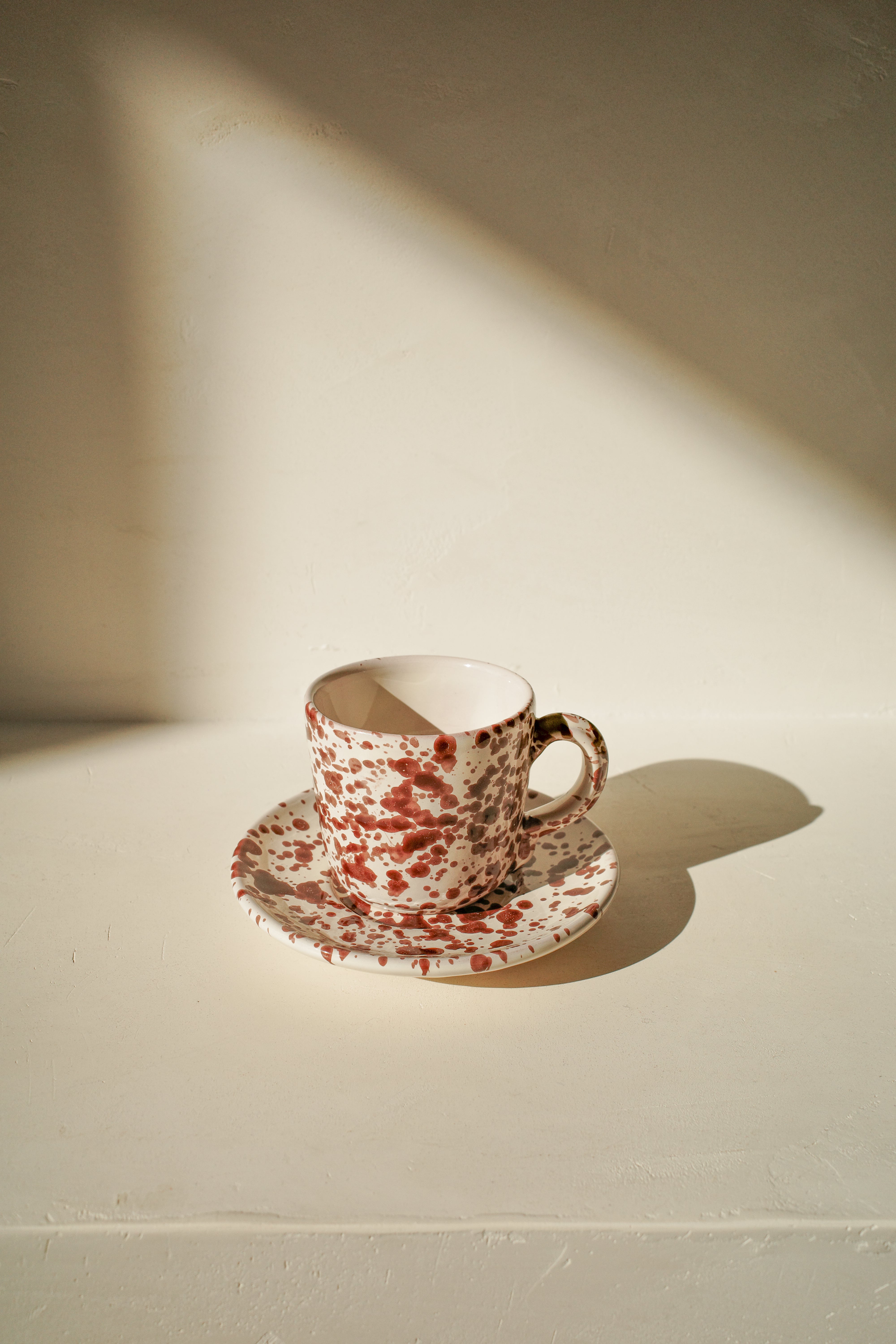 Ceramic cup and saucer with white glaze and brown splatter pattern.