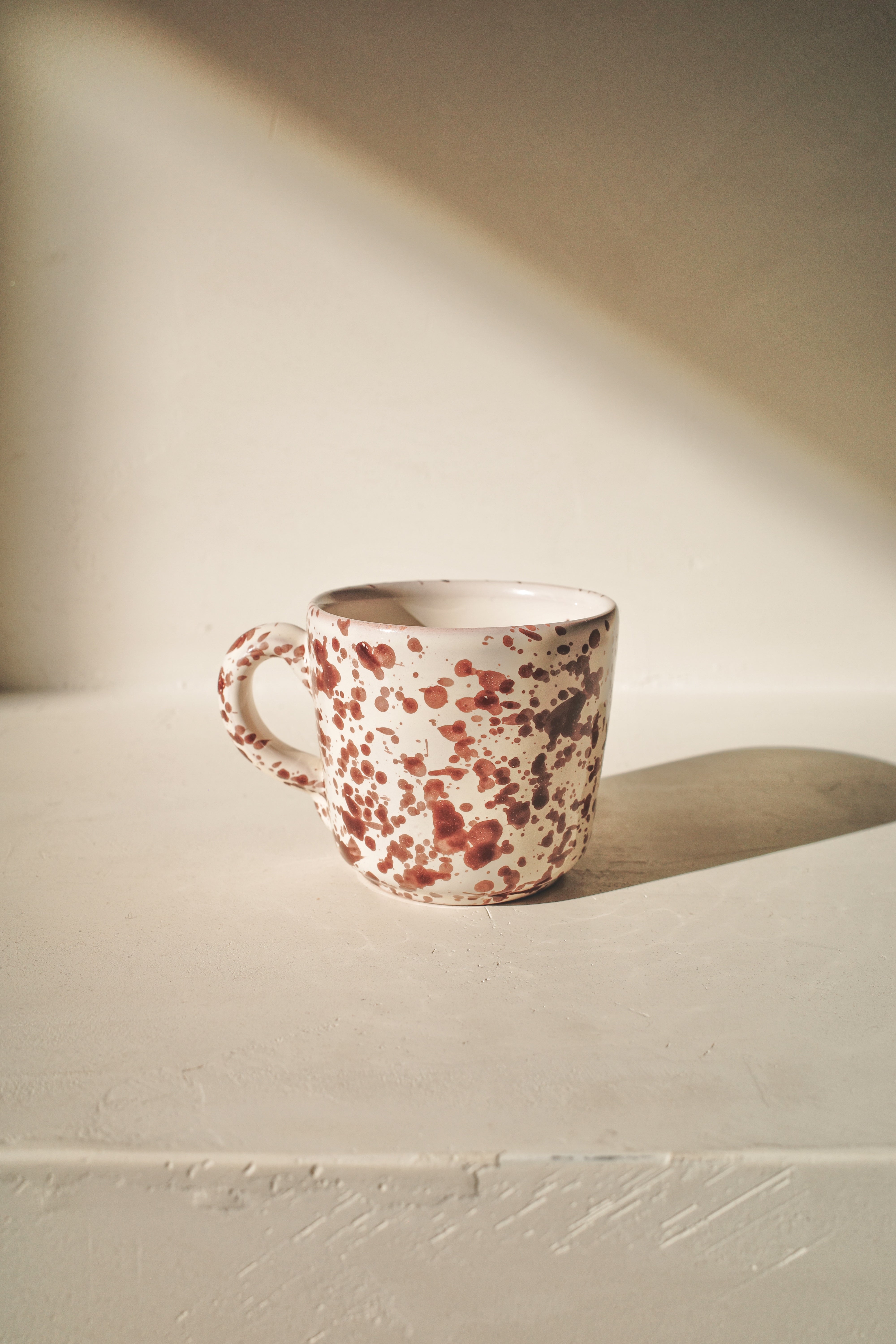 Ceramic cup with white glaze and brown splatter pattern.