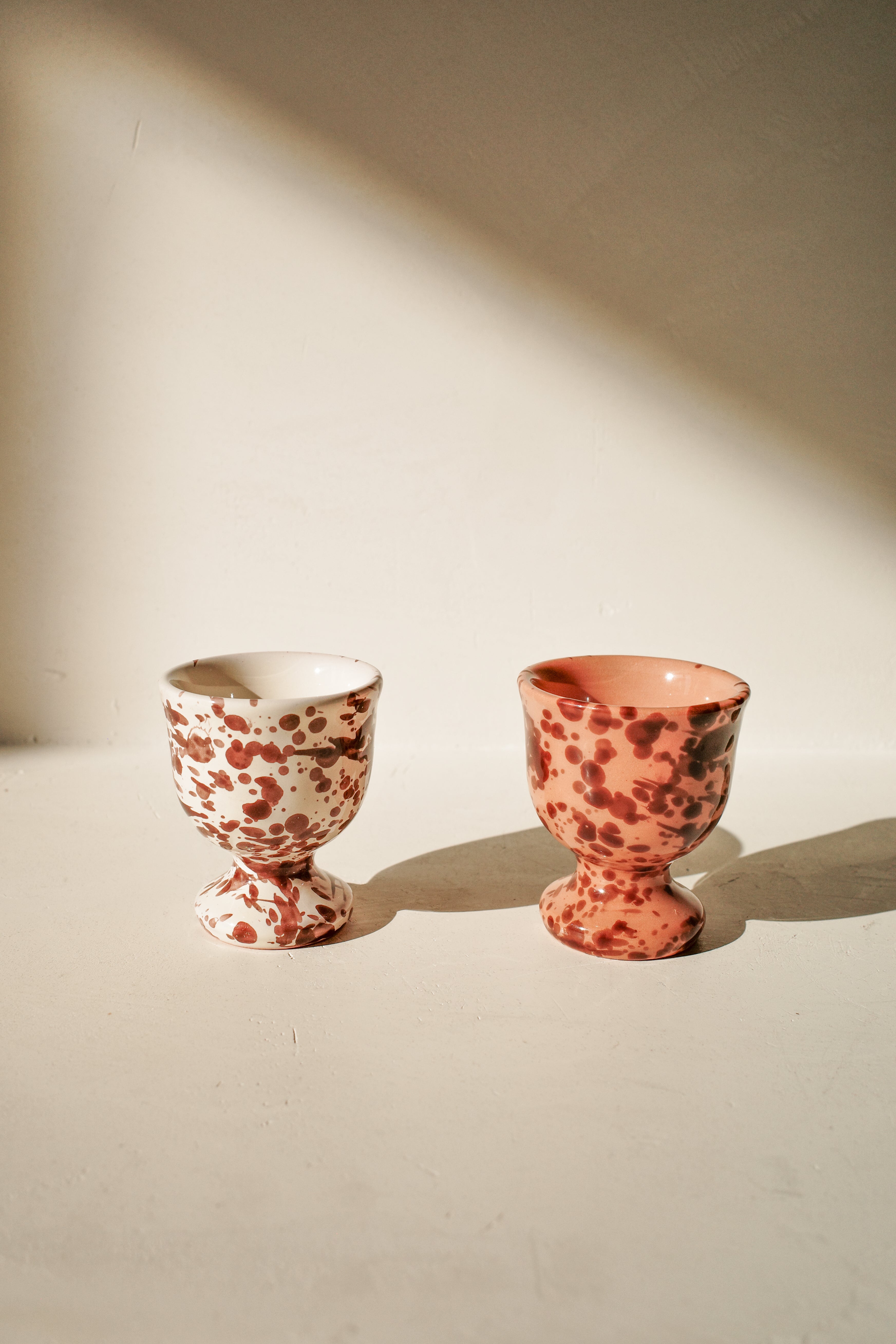 Ceramic egg cups with white or terracotta glaze and brown splatter pattern.