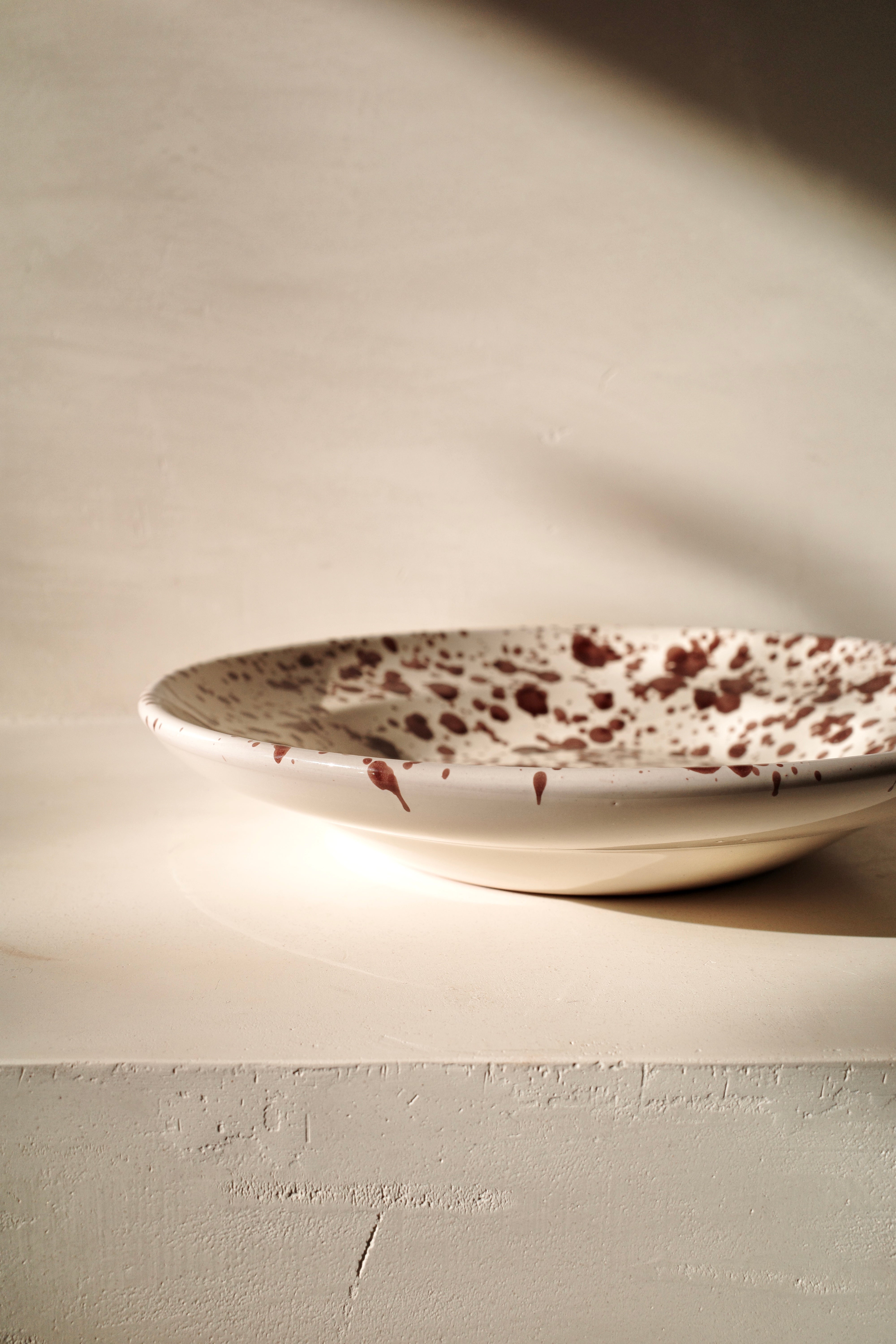 Ceramic deep plate with white glaze and dark brown paint splatter.