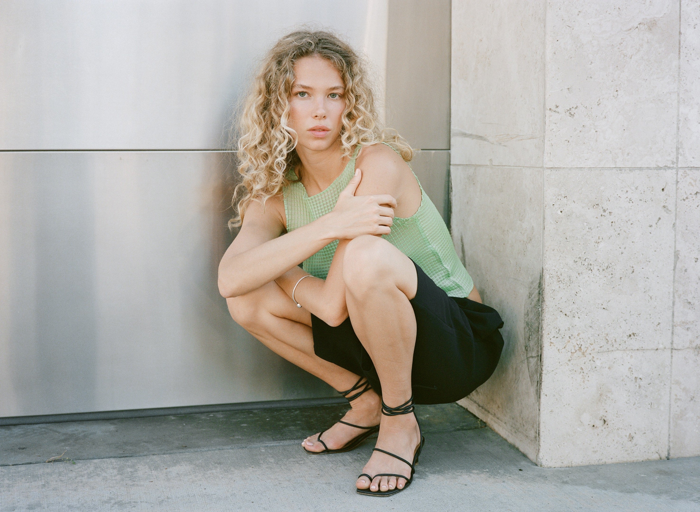 Woman sitting against a wall wearing black strappy sandals