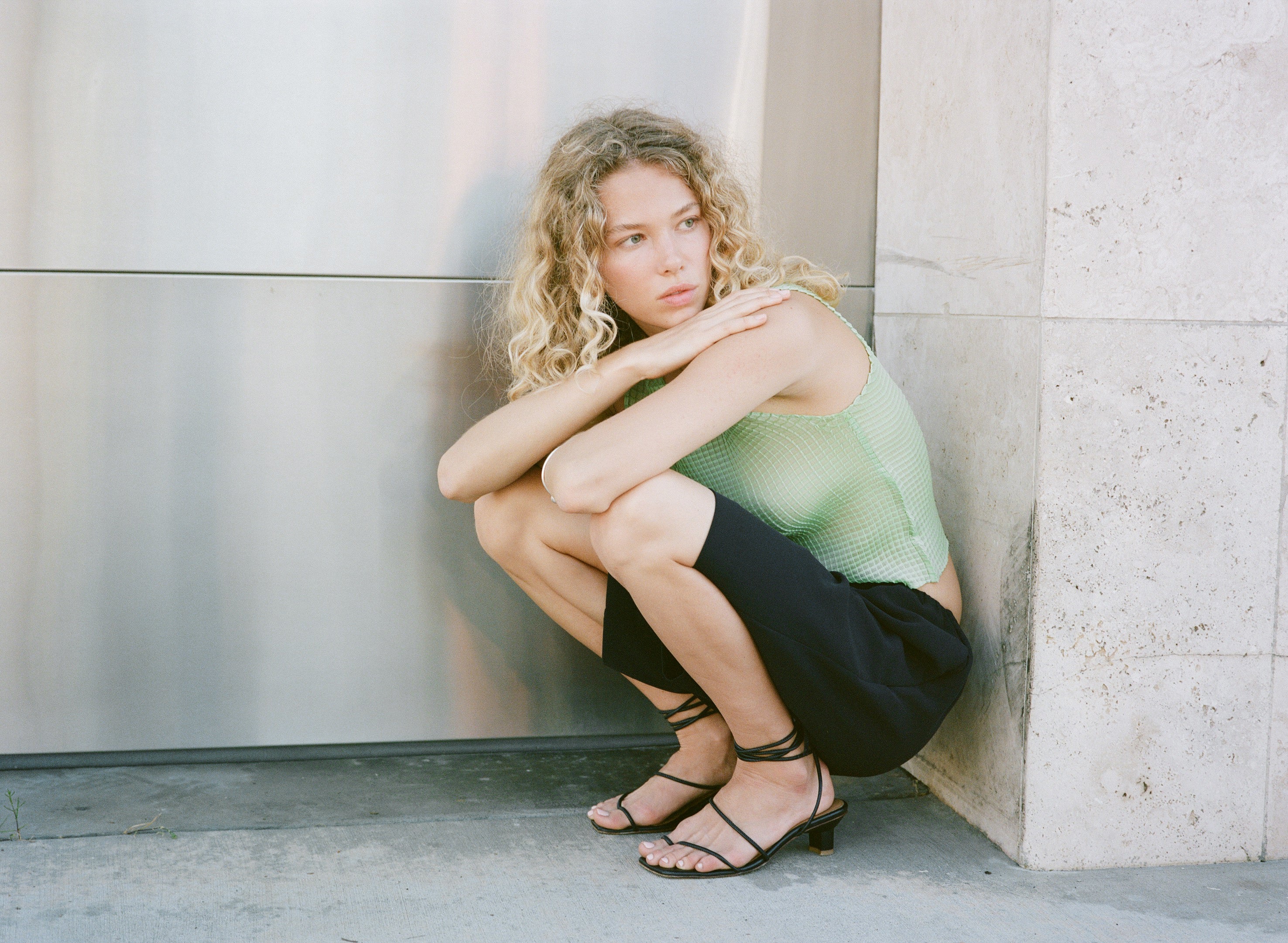 Woman sitting against a wall wearing strappy sandals