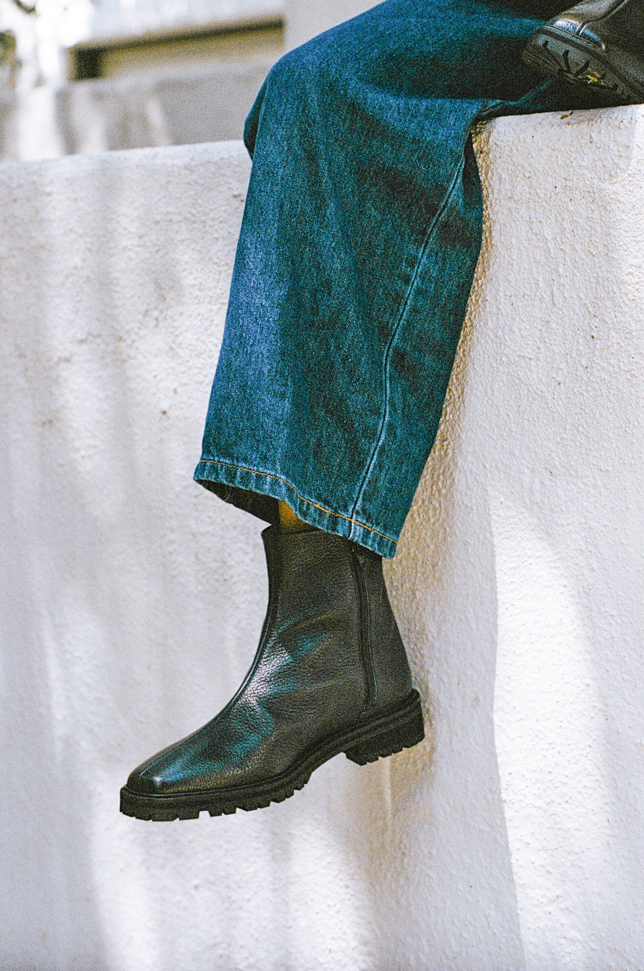 Model wears black tumble leather ankle boot with rubber tread sole and side zipper.