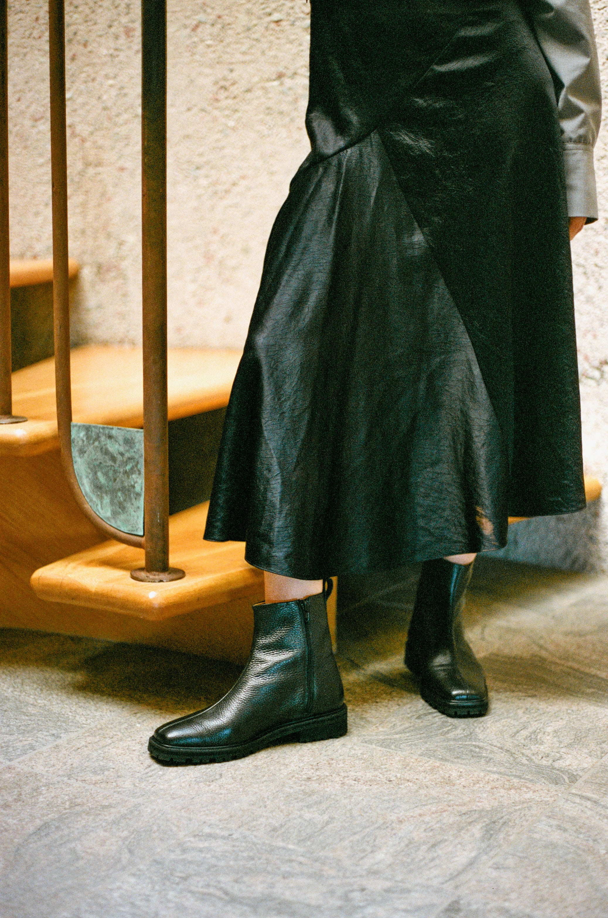 Model wears black tumble leather ankle boot with rubber tread sole and side zipper.