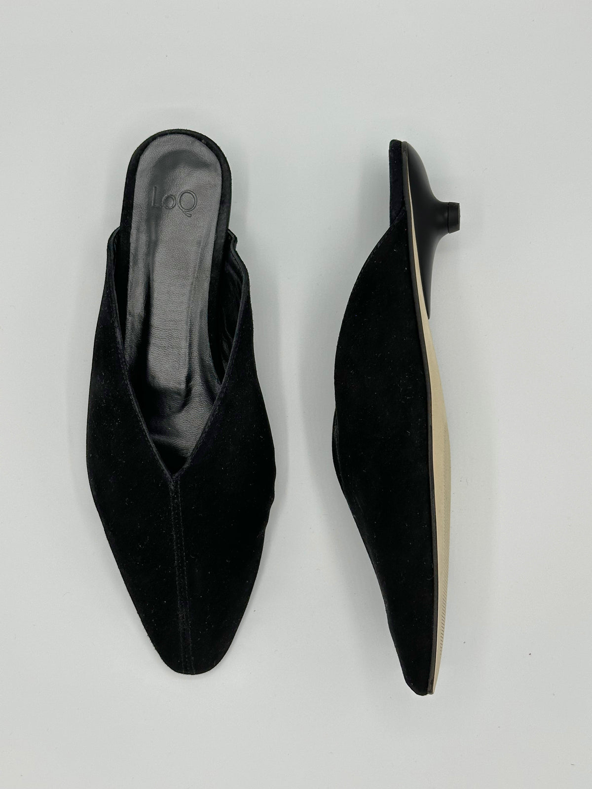 A pair of black pointed-toe mule heels shown from the top and side against a light gray background.