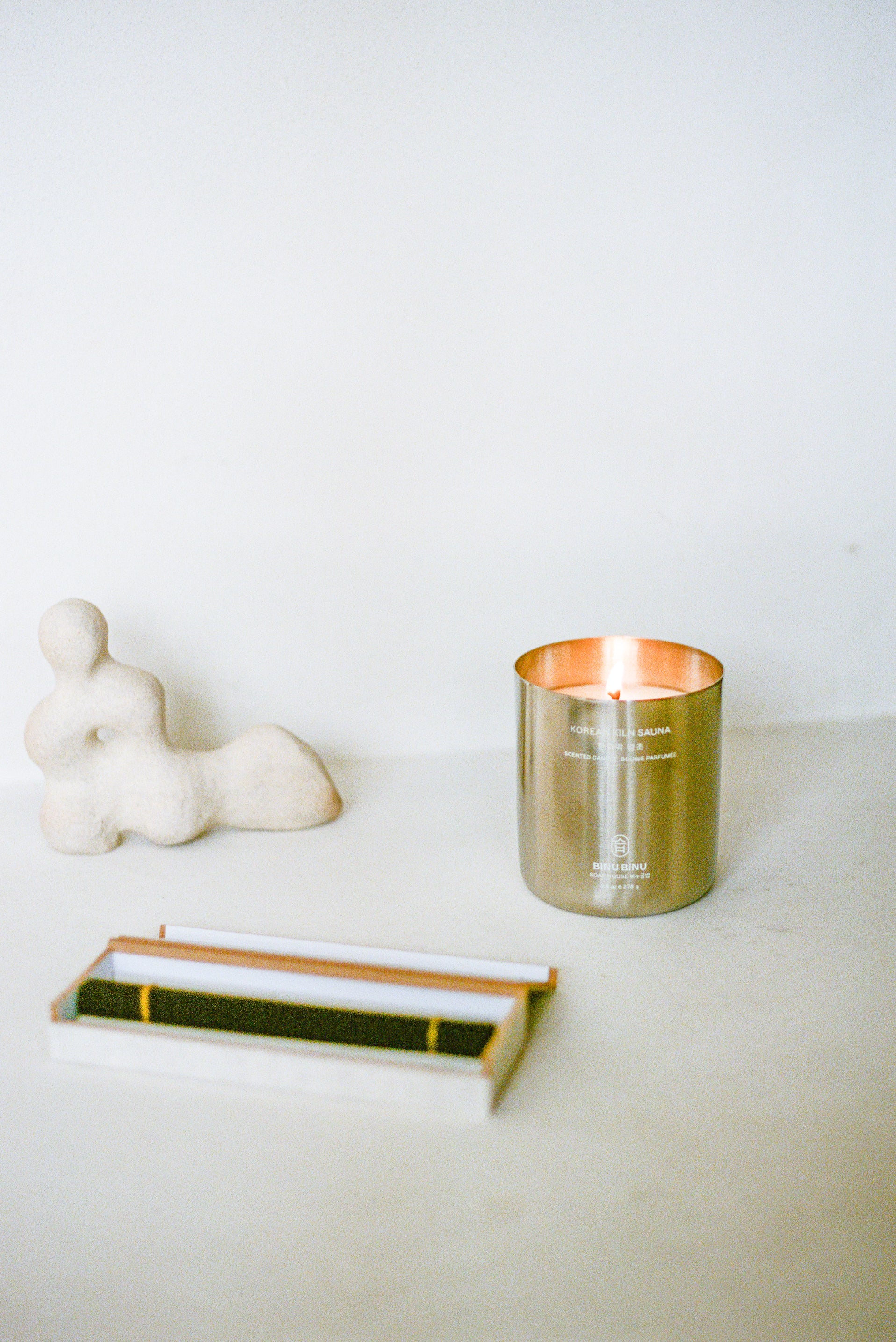 Candle in metal container on surface with incense and sculpture.