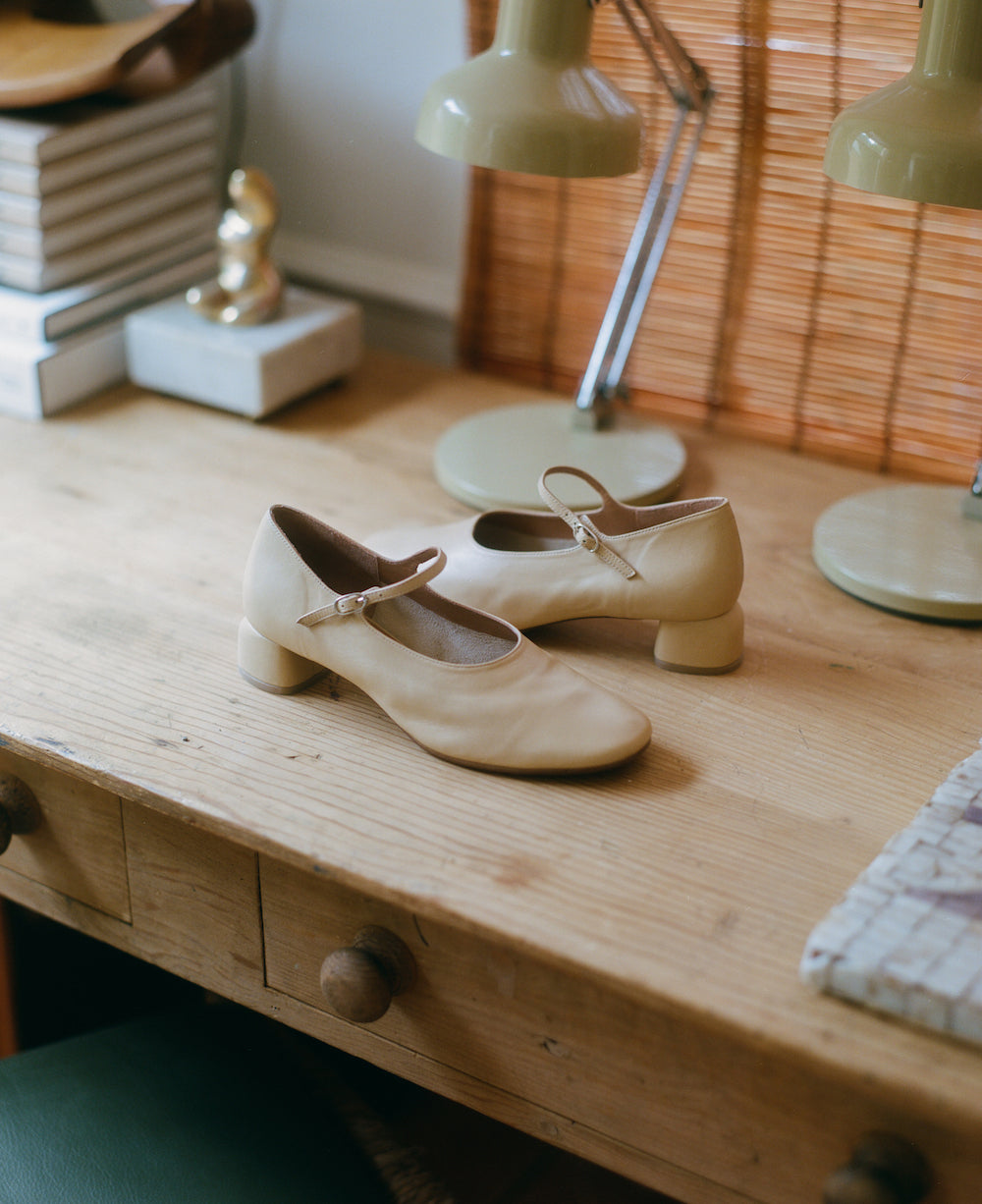 Modern Mary Jane featuring a classic silver buckle with an updated round heel in biscuit beige leather. Round toe and 1" covered heel.