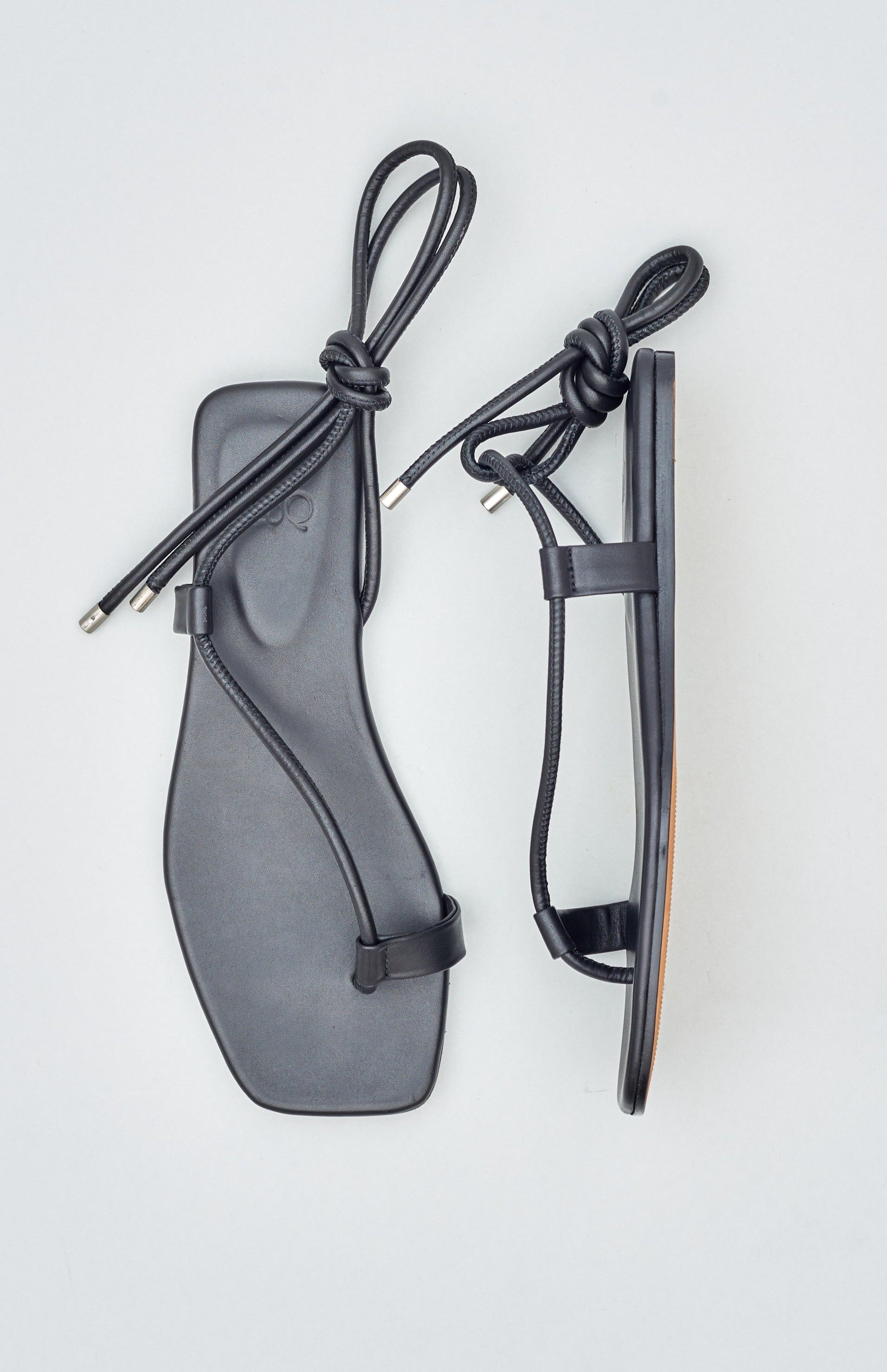 Minimal sandals with an adjustable toe ring threaded with black tubular leather straps that wrap around the ankle.