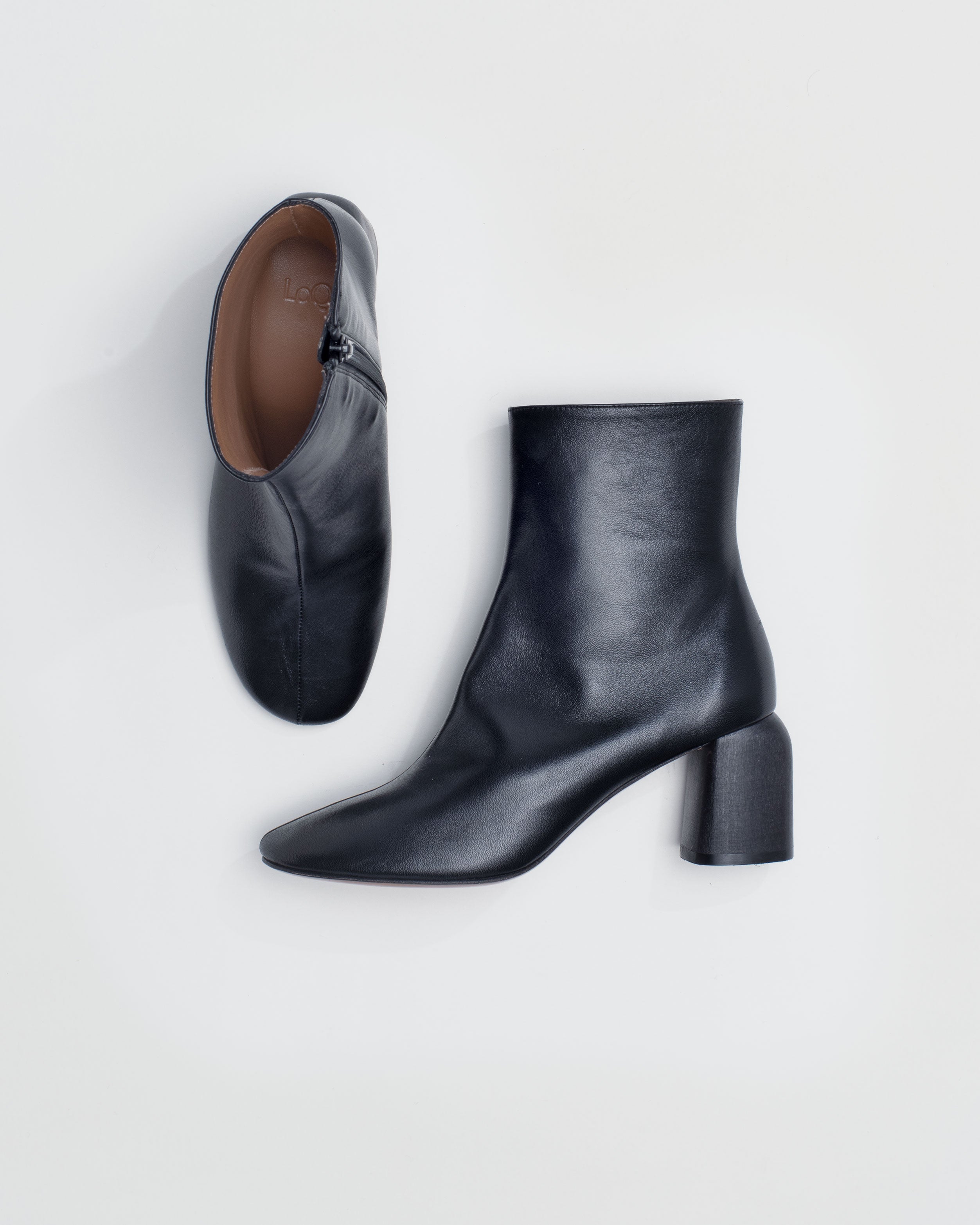 Model wears round toe ankle boot in buttery black leather with a carved sculptural heel. Glove-like fit with inner side zip closure. 2 ½" polished wood heel.