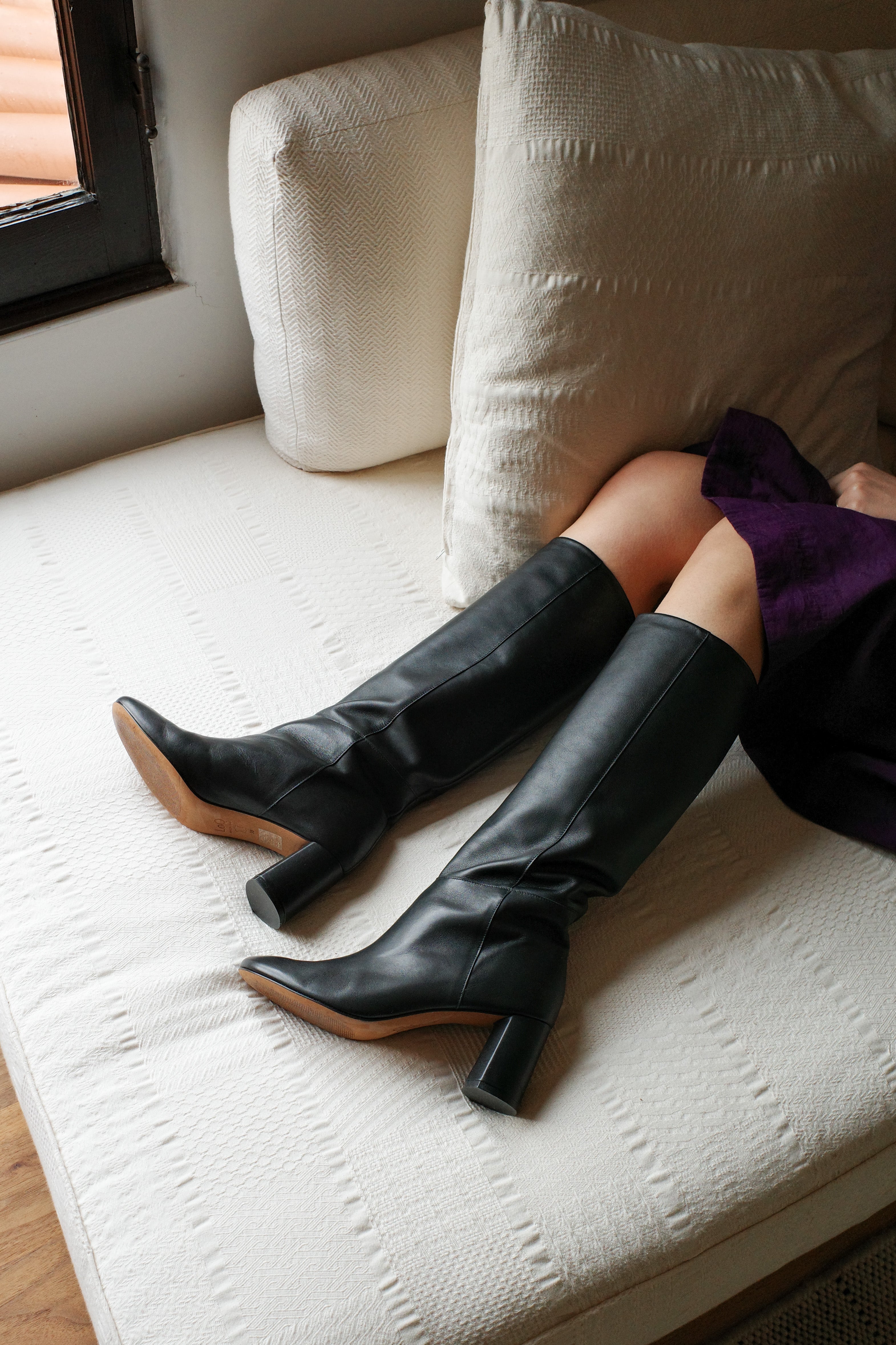 Model wears tall pull-on boot in a supple classic black leather that sits below the knee with a round toe