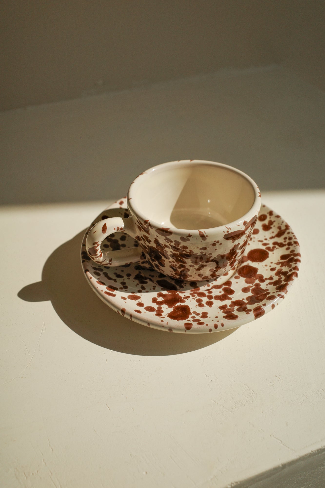 Ceramic espresso cup and saucer with white glaze and dark brown splatter pattern.