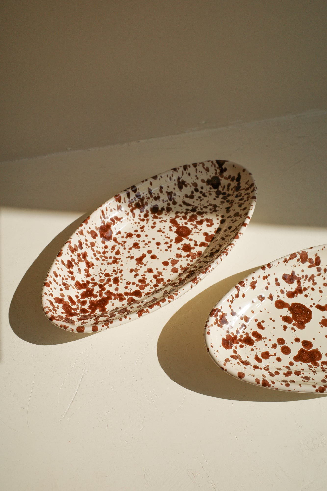 Ceramic oval plate with white glaze and dark brown paint splatter.