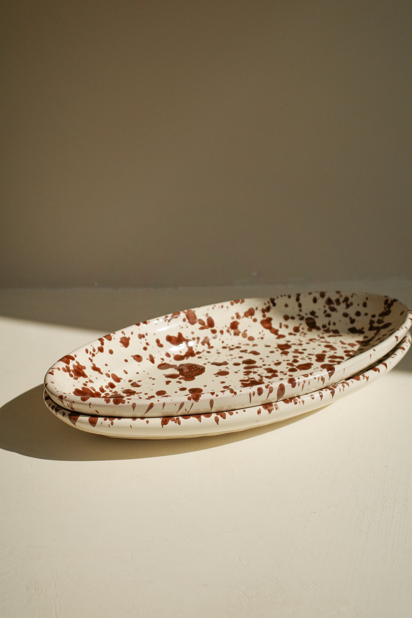 Ceramic oval plate with white glaze and dark brown paint splatter.