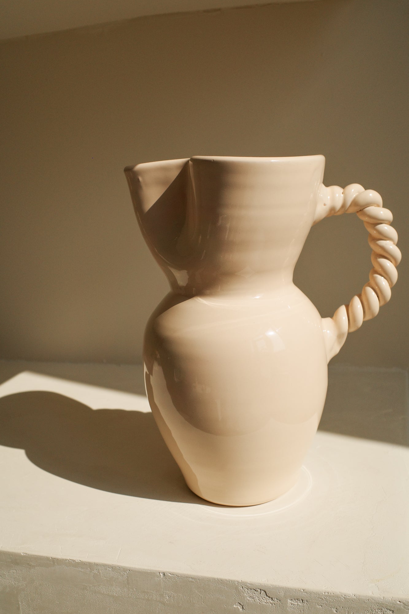 Cream glazed ceramic pitcher with pinched spout and braided handle.