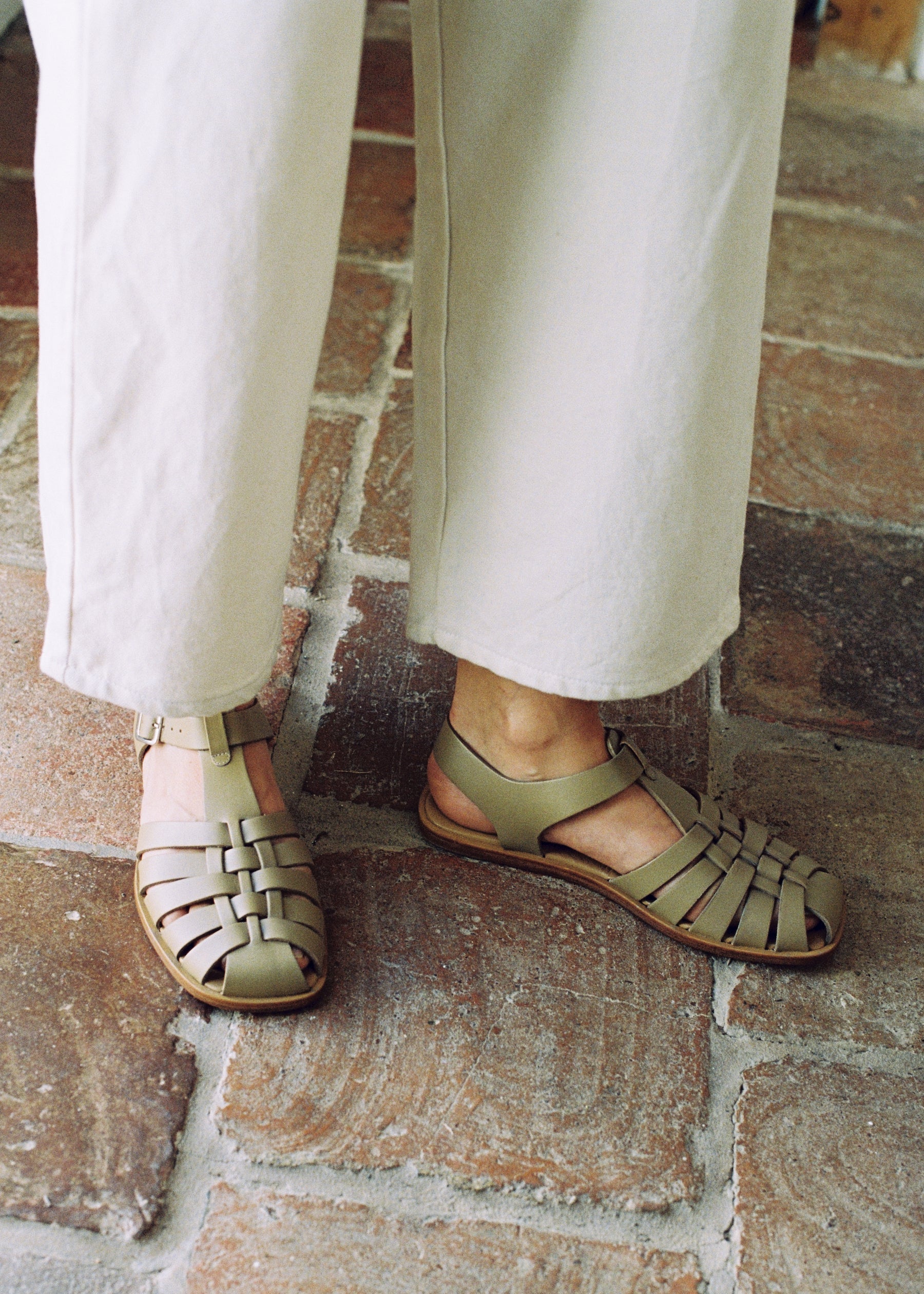 Model wears fisherman sandal with a buckled closure and t-bar vamp in taupe leather. Vegetable-tanned leather upper and outsole.