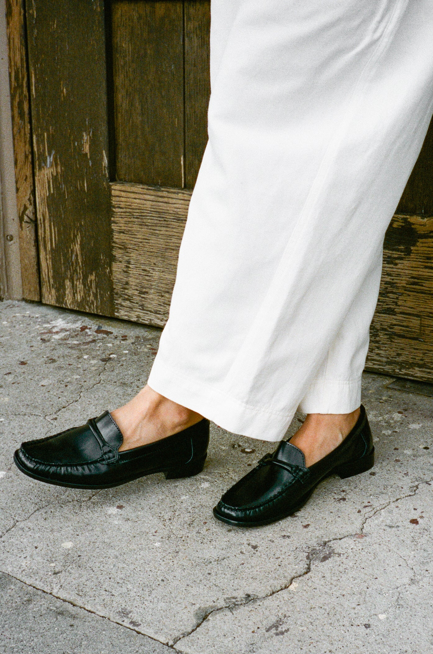 Model wears black leather loafer with tubular strap.