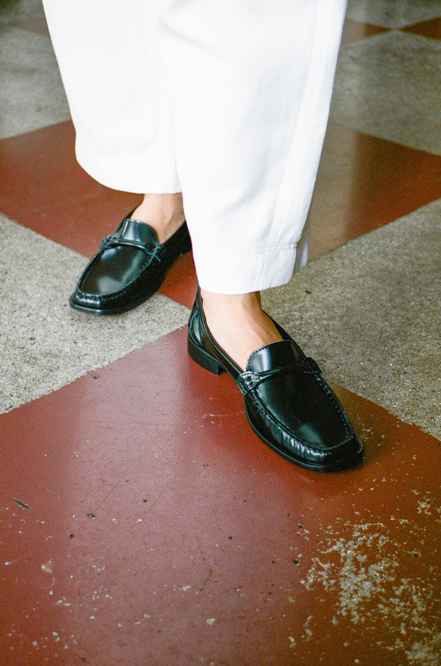 Model wears black leather loafer with tubular strap.