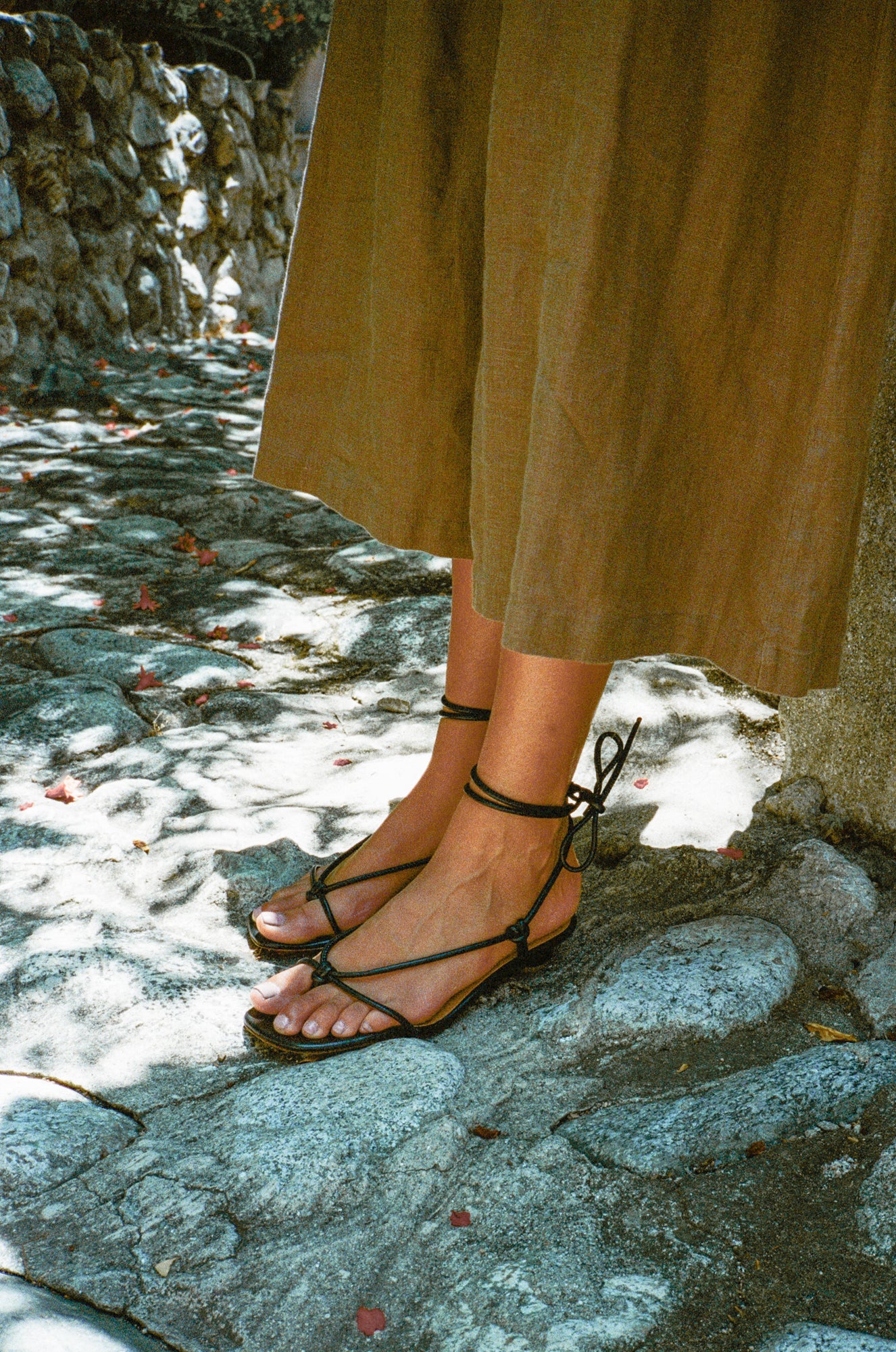 Model wears knotted thong sandal featuring a short heel and tubular black leather straps that wrap around the ankle to tie.