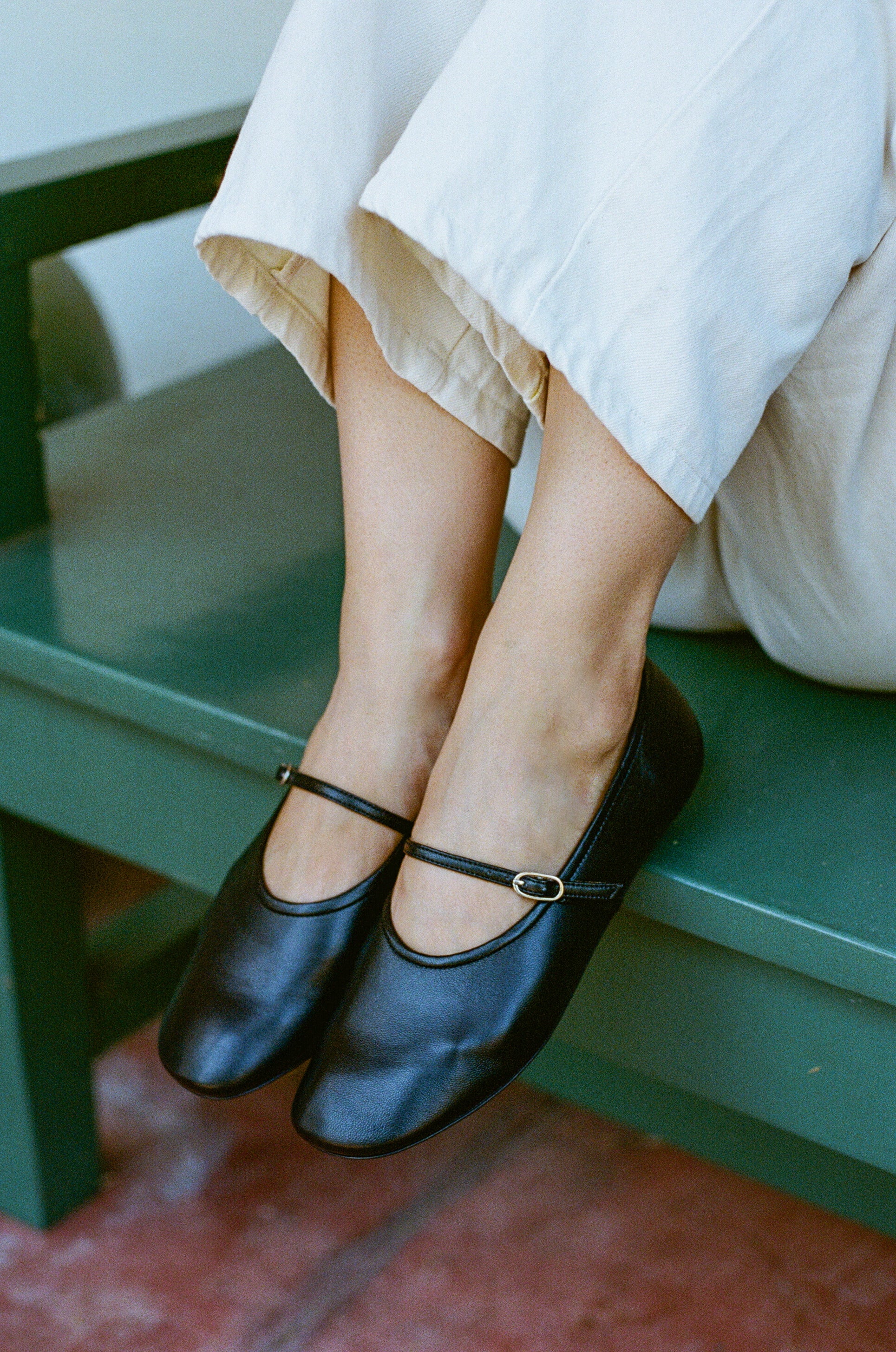 Model wears black leather mary jane style flat shoe with strap and buckle closure.