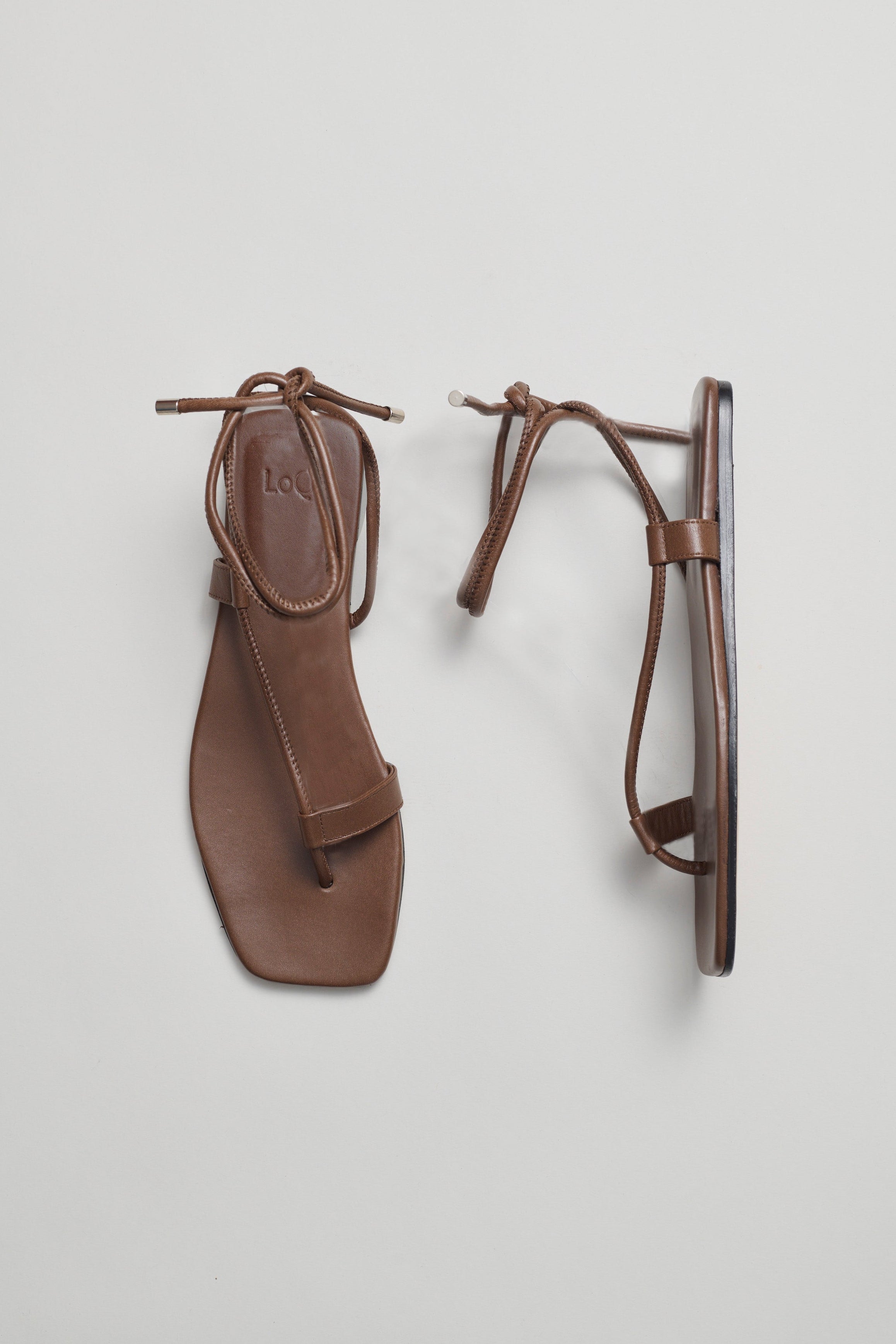 Brown sandals with ankle wrap straps on a light gray background
