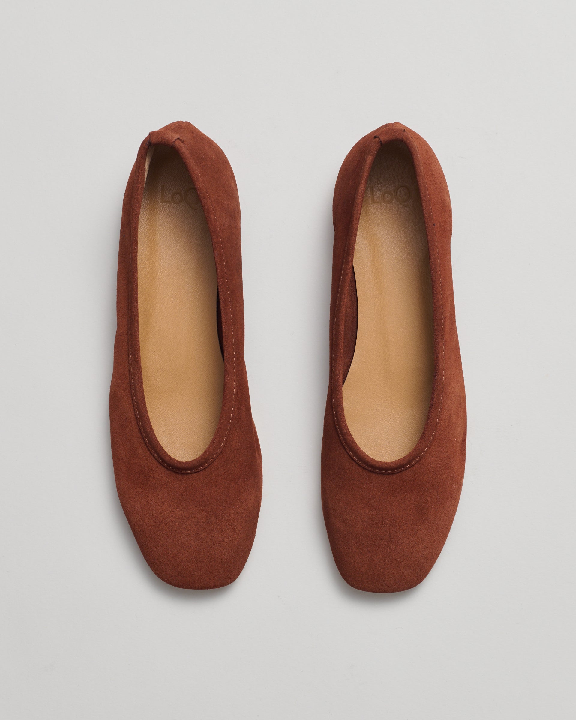 A pair of rust-brown suede ballet flats shown from a top-down view on a light gray background.